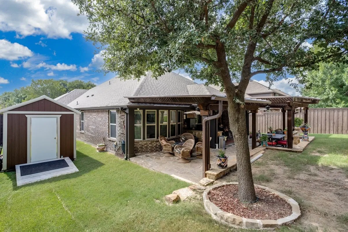 Expansive backyard featuring a stone patio, large pergola, and mature trees