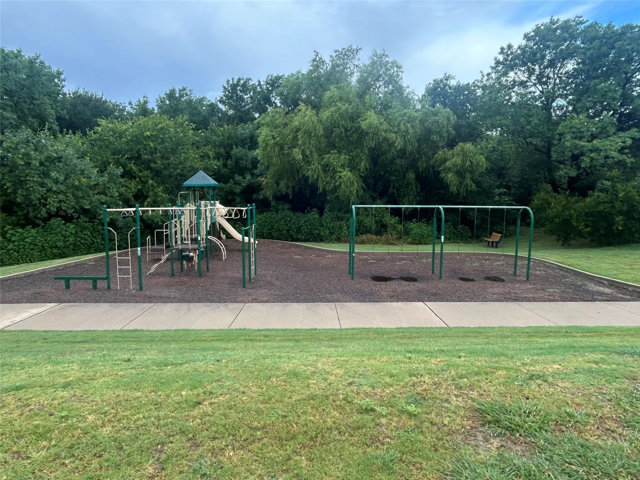 Community playground with a multi-level play structure, swing sets, and a soft ground covering
