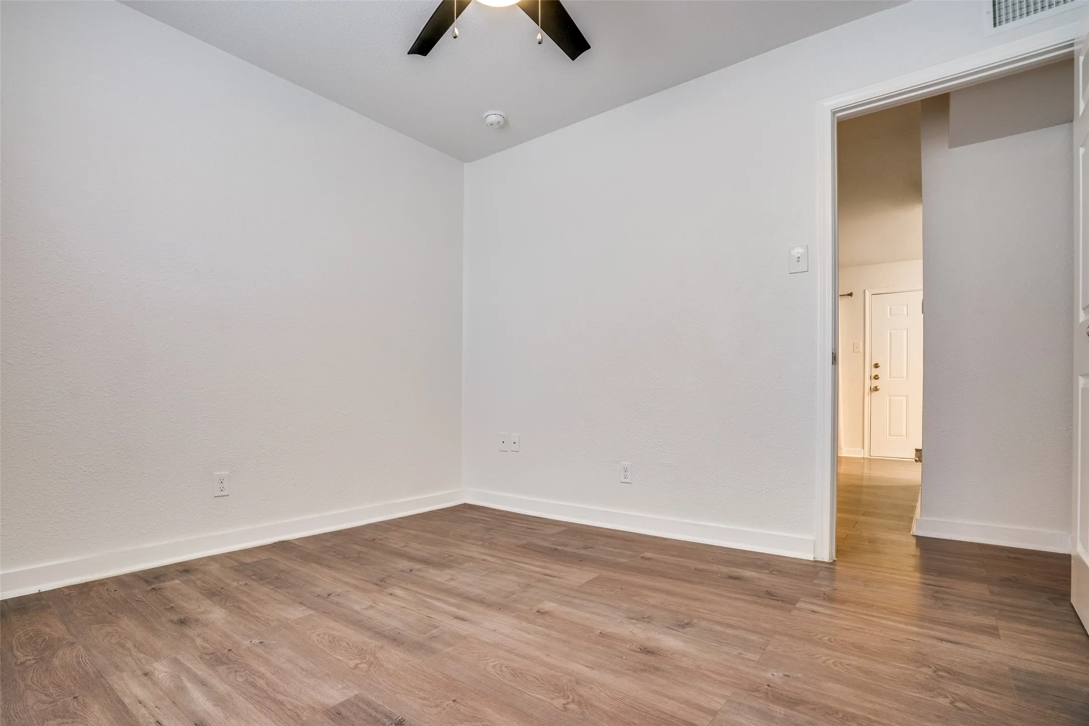Spacious interior room featuring wood-finish flooring, white baseboards, and a contemporary ceiling fan