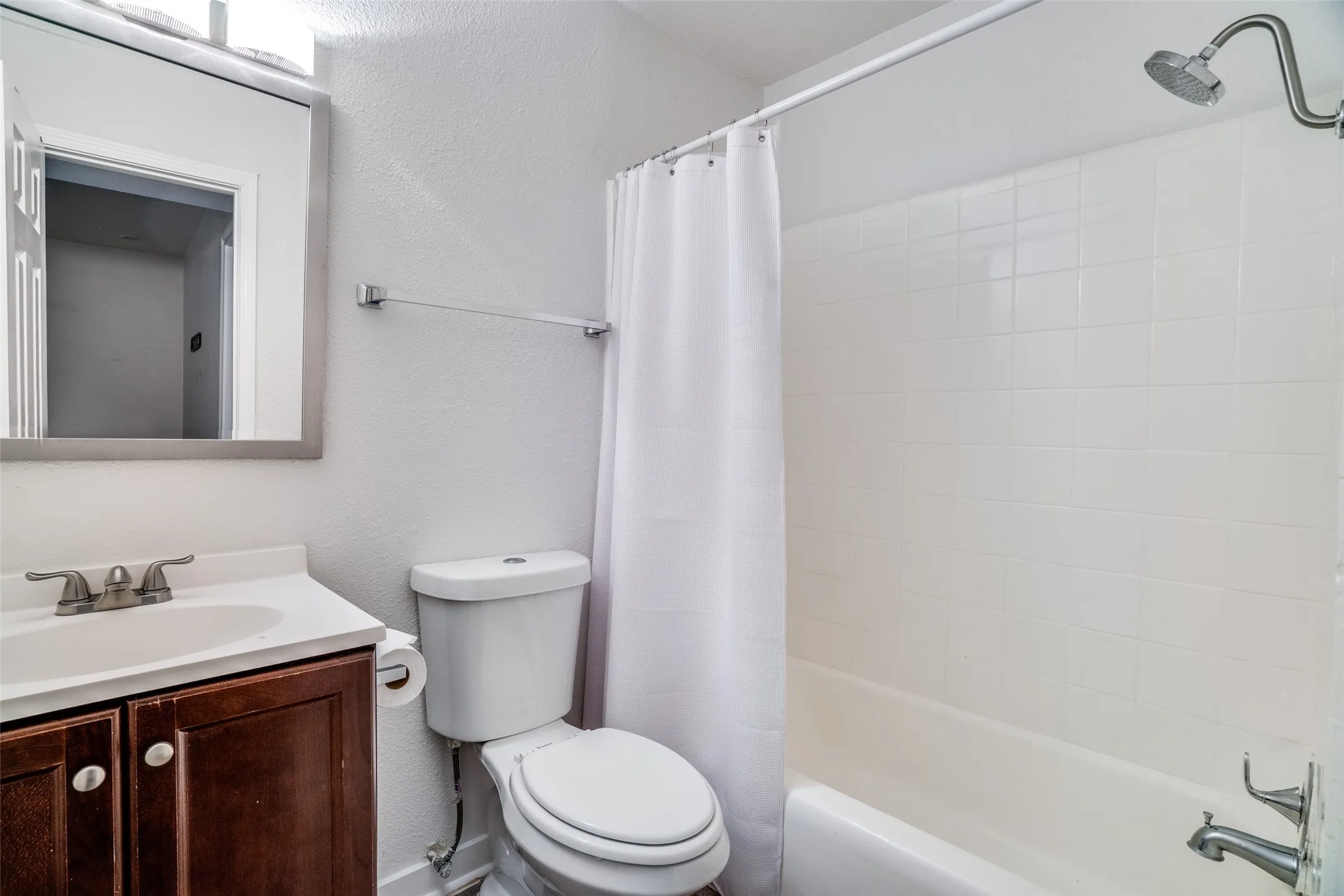 Bathroom featuring a white subway-tiled shower, a white porcelain tub, and a dark wood-finish vanity with a white countertop sink