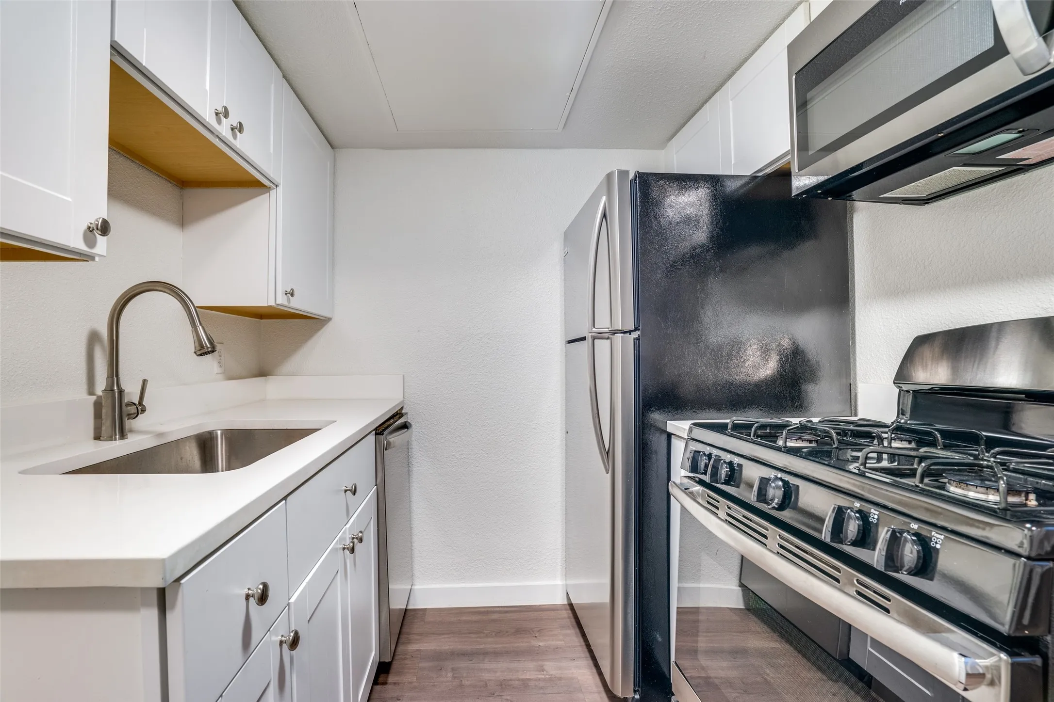 Compact kitchen featuring stainless steel appliances, white cabinetry with silver hardware, white countertops, and wood-finish flooring