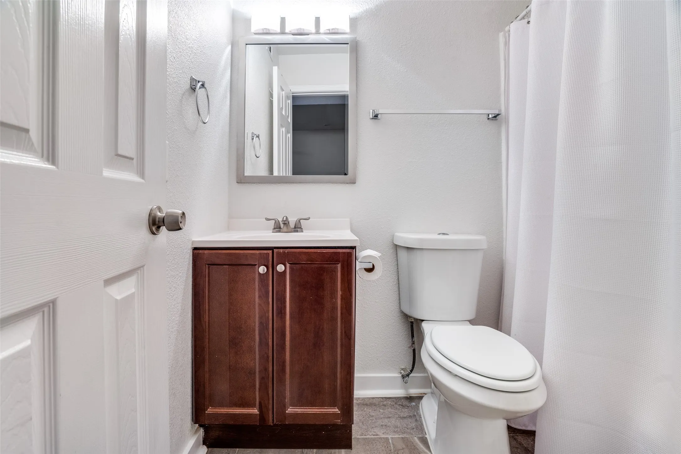Bathroom featuring wood-finish vanity with white countertop, chrome fixtures, framed mirror, and tile flooring