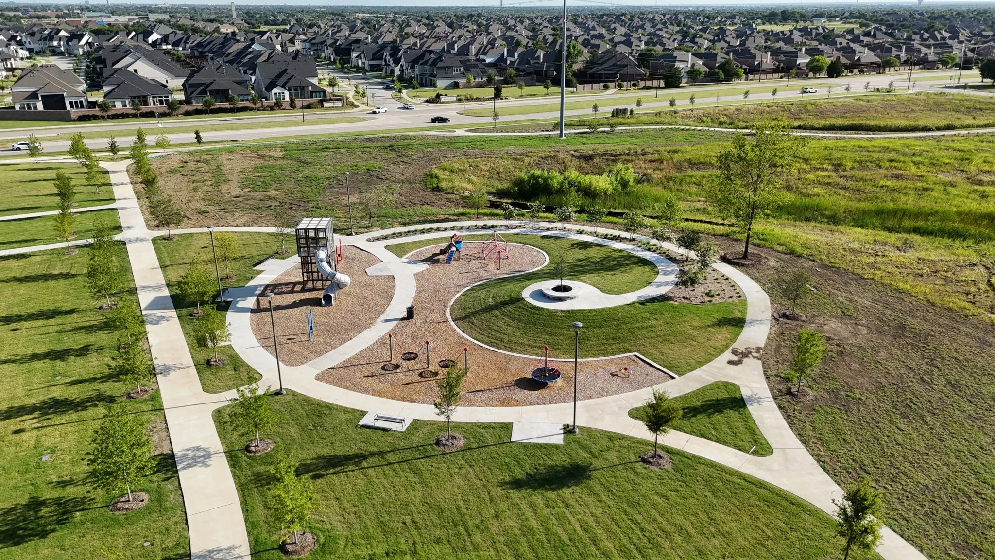 Expansive park grounds featuring a modern play structure, dedicated walking paths, mature trees, and open green spaces