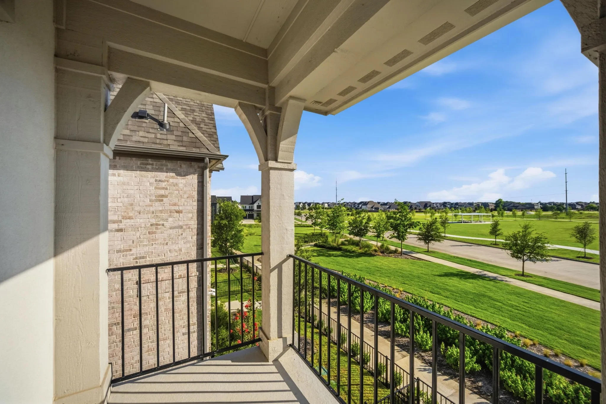 Covered balcony off the primary bedroom, featuring decorative columns, an arched ceiling, and black wrought iron railing