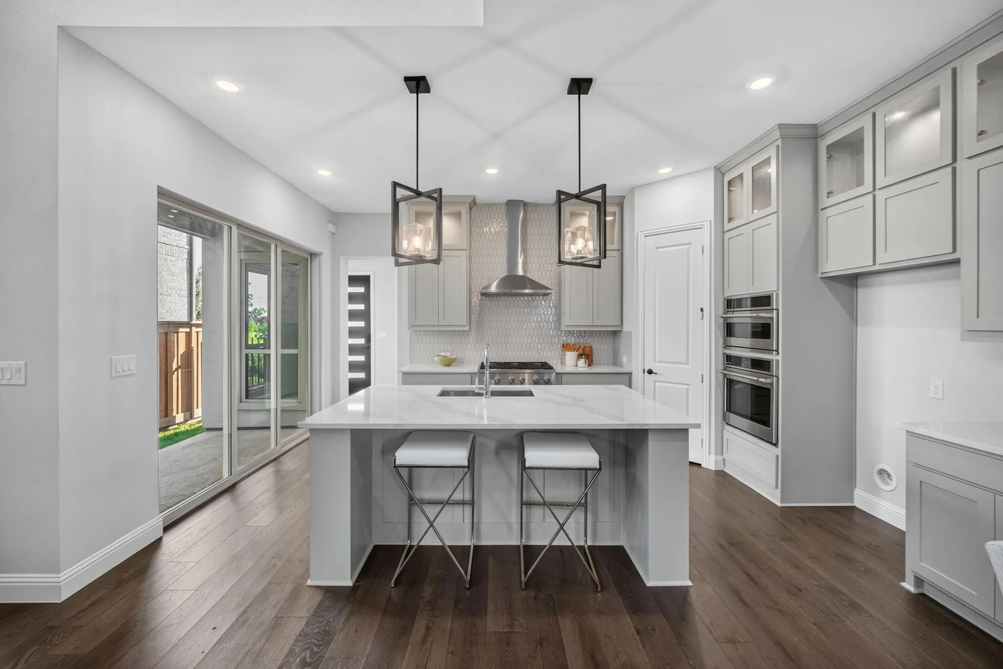Modern kitchen featuring a central island with a sink and white countertop, light gray cabinetry, stainless steel appliances, and wood-finish flooring