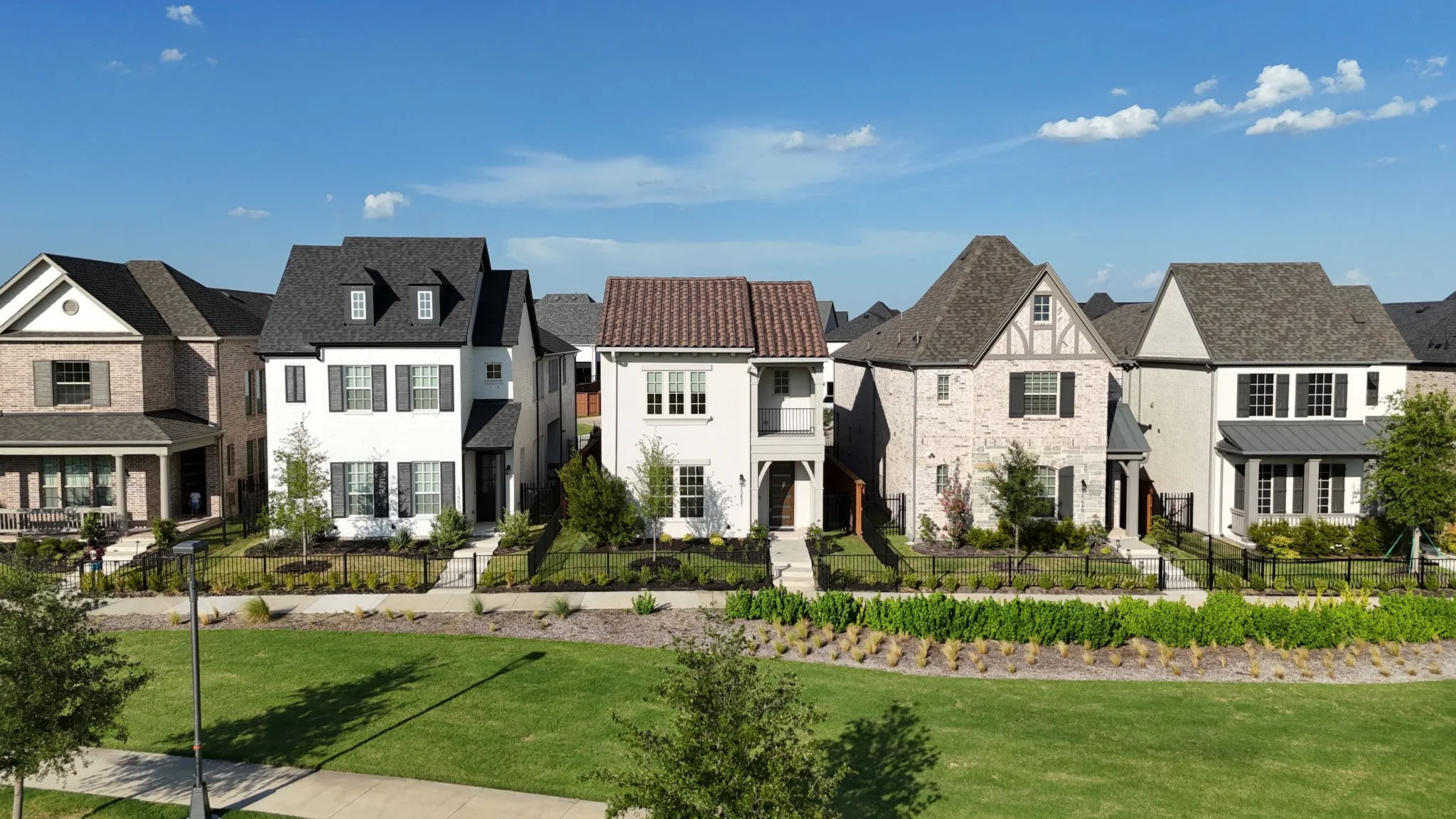 White two-story residence featuring black shutters, a dark shingled roof with dormer windows, and a paved walkway leading to the front entry