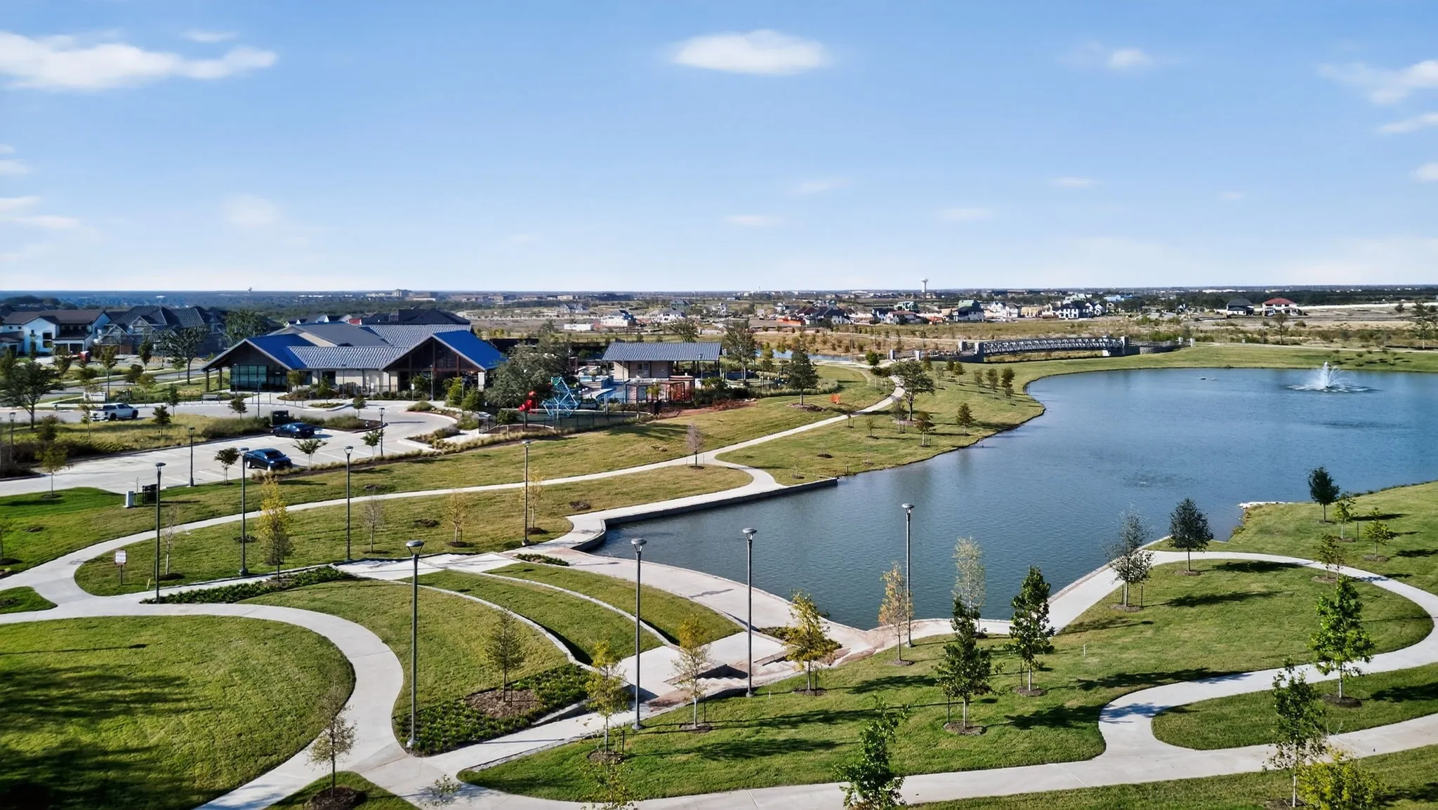Expansive community amenities including a large lake with a central fountain, a modern clubhouse building, and multiple curved walking paths