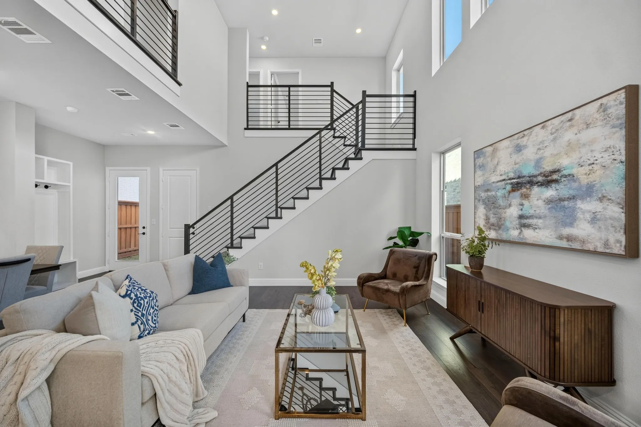 Two-story living area featuring beautiful wood-finish flooring, a contemporary staircase with black railings, and an open-concept upper-level balcony
