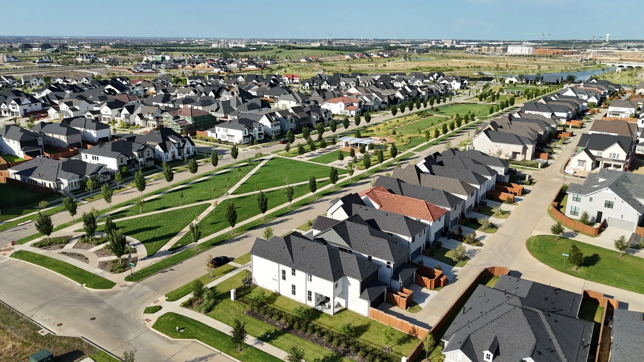 Contemporary residential development featuring a manicured central park, extensive green spaces, a variety of architectural styles, paved roadways, and integrated pedestrian pathways