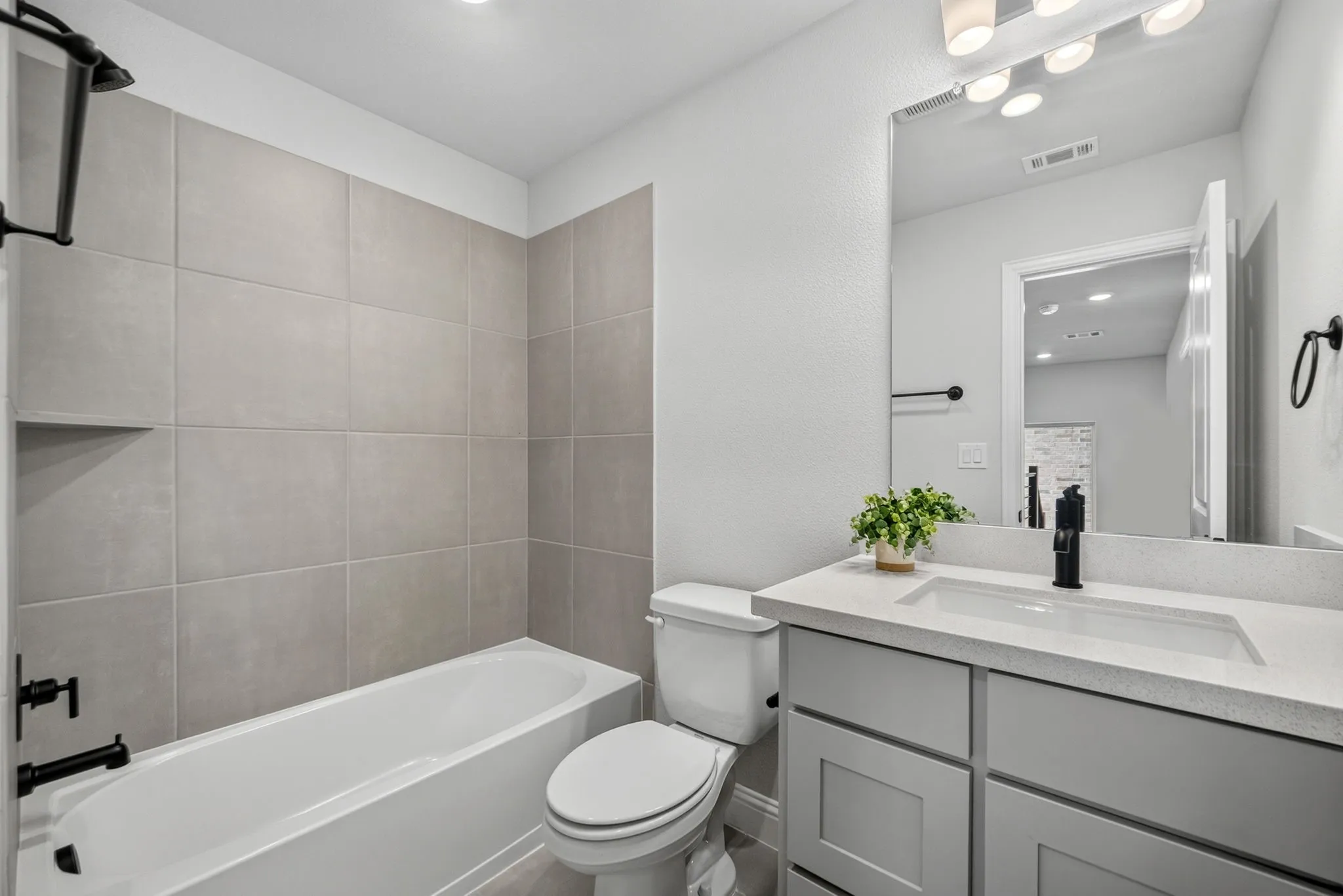 Bathroom featuring a tub/shower combination with large format grey tiling, built-in shower niche, and matte black fixtures
