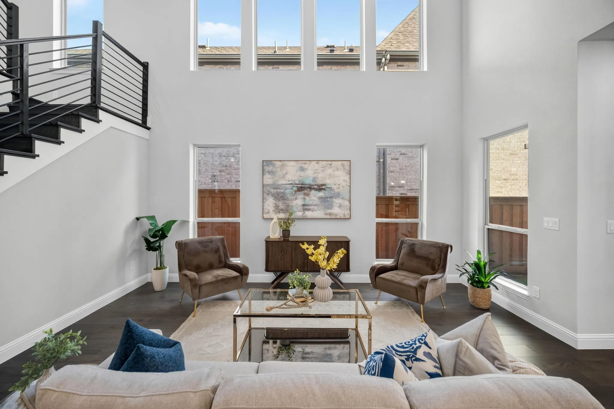 Vaulted ceiling living room featuring a contemporary open-tread staircase with black metal railings, wood-finish flooring, and multiple large windows providing ample natural light