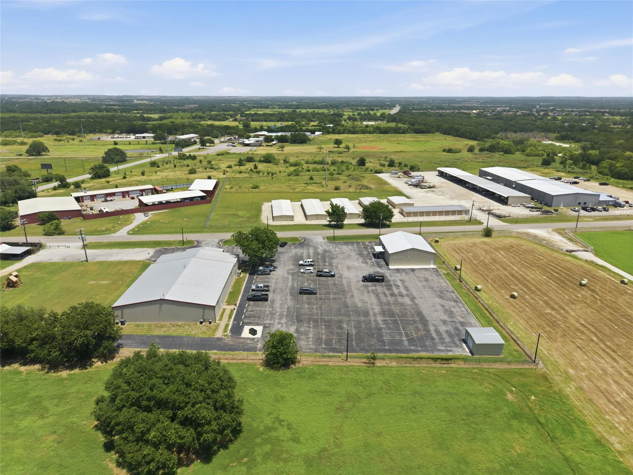 Aerial property overview featuring multiple commercial structures, expansive paved parking areas, and surrounding green spaces