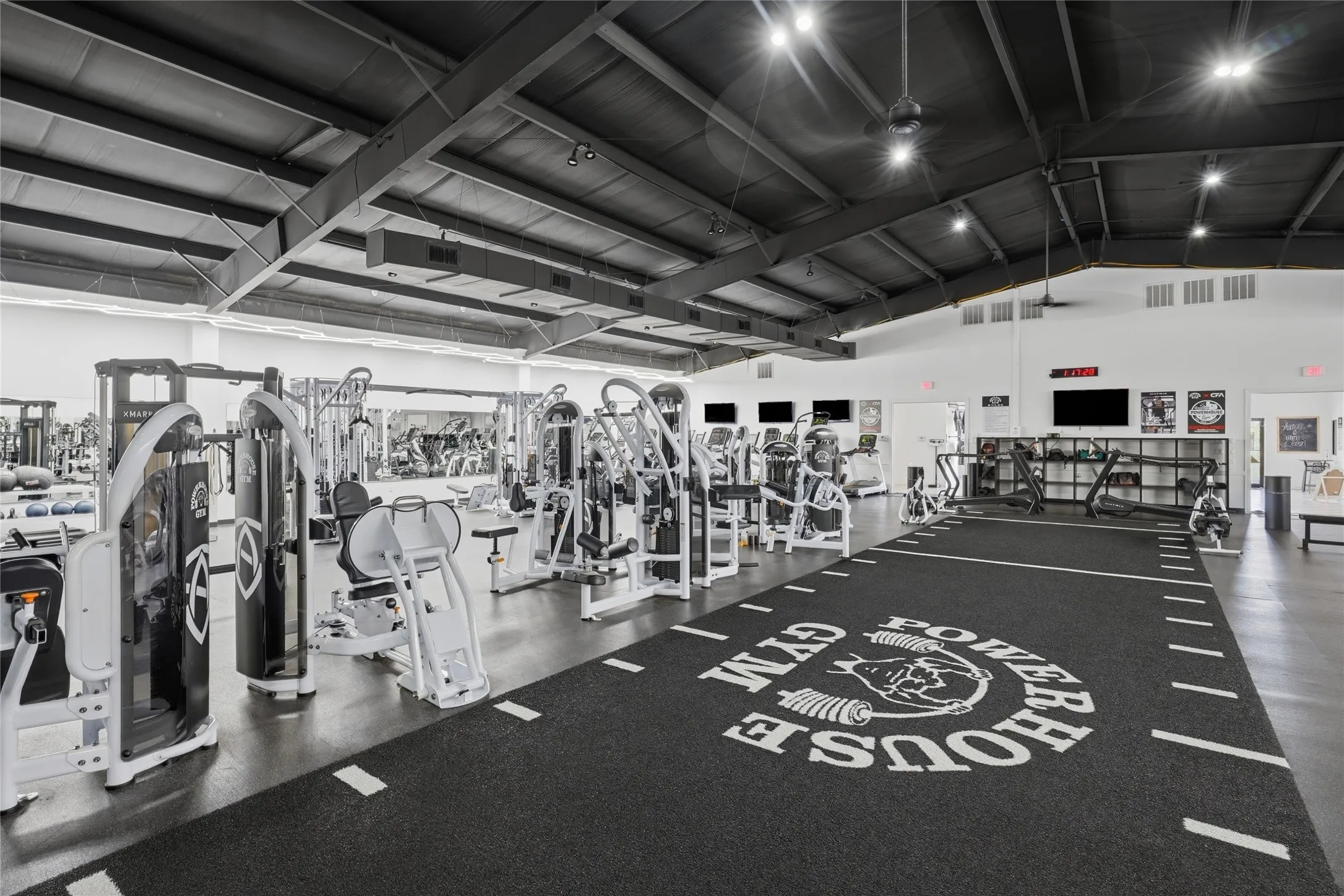 Spacious fitness area featuring a dark, textured floor with white markings and a large central logo