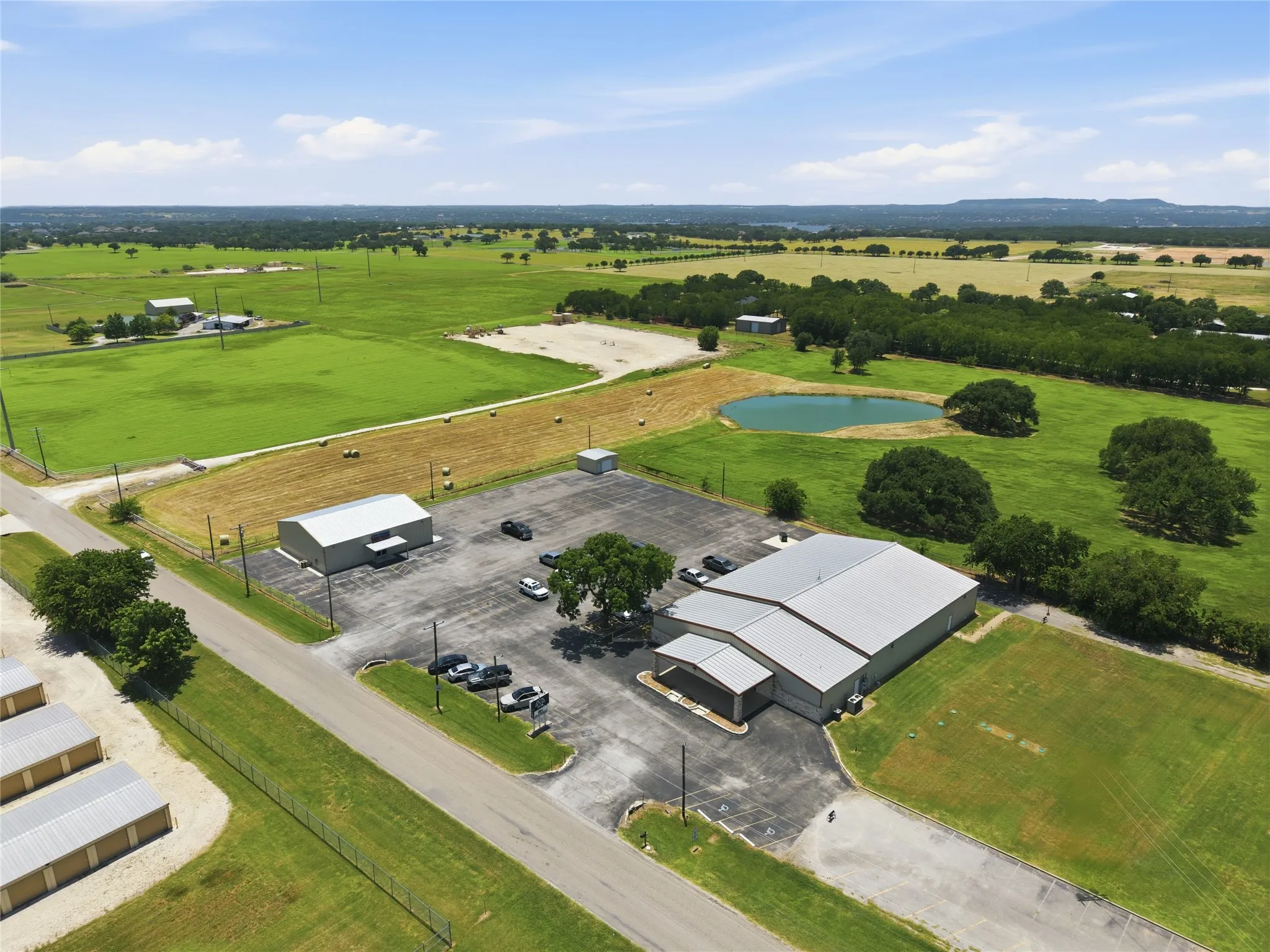 Expansive commercial property featuring multiple metal-roof buildings, a large paved parking area, and surrounding green acreage