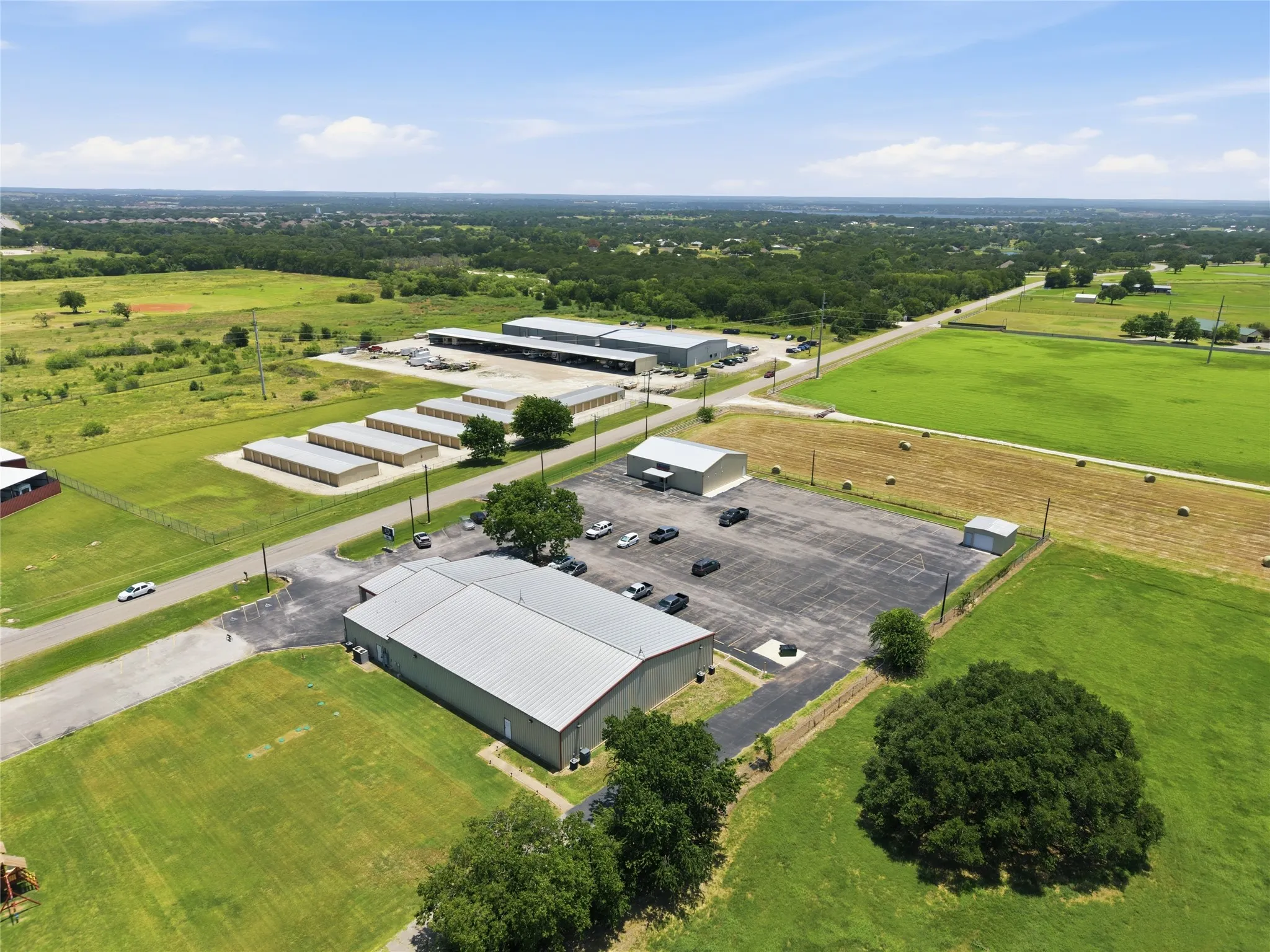 Commercial property featuring multiple buildings with metal roofs, extensive paved parking, and visible acreage