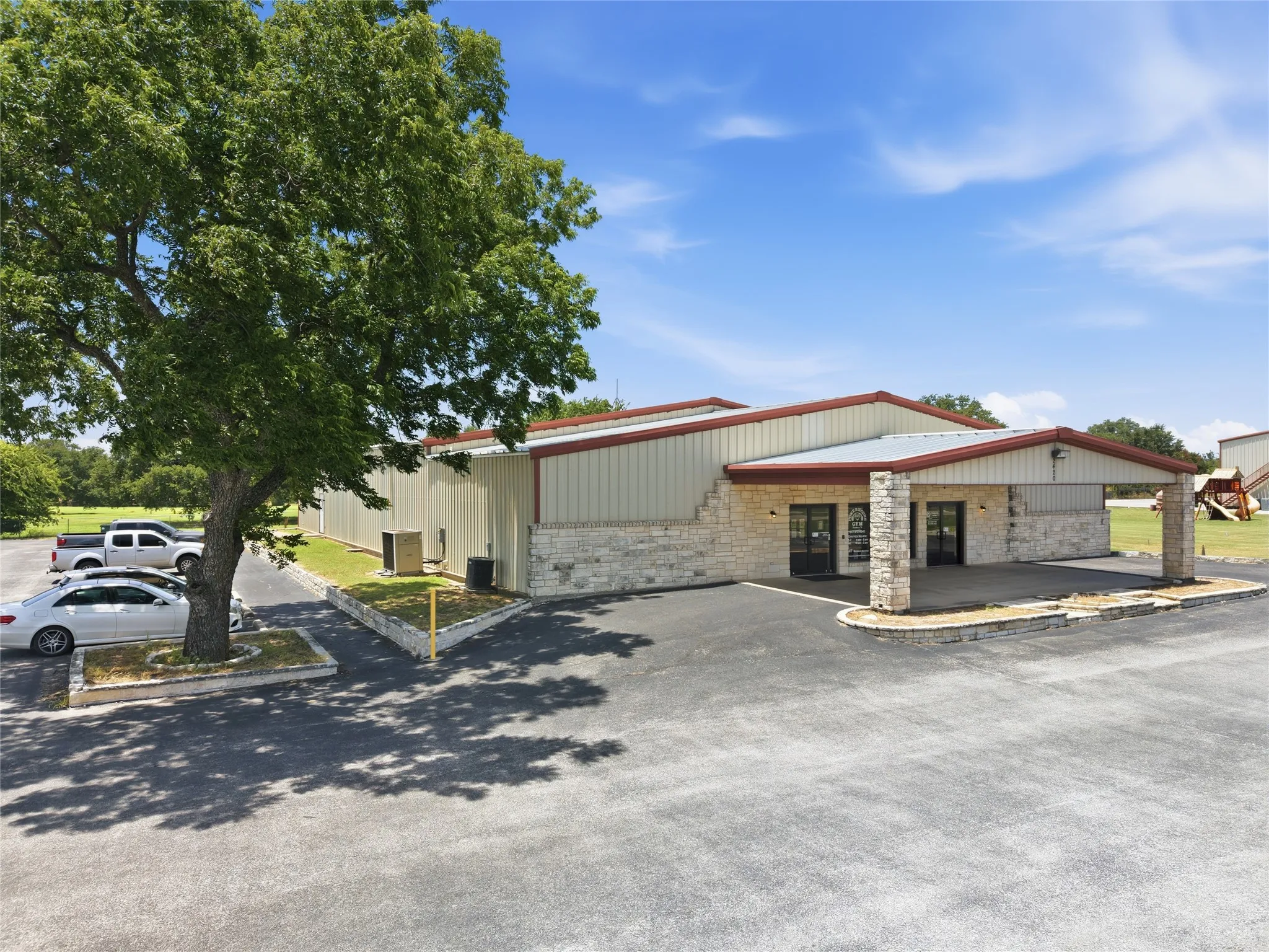 Commercial building featuring a stone and metal panel exterior, covered entry, and expansive paved parking area
