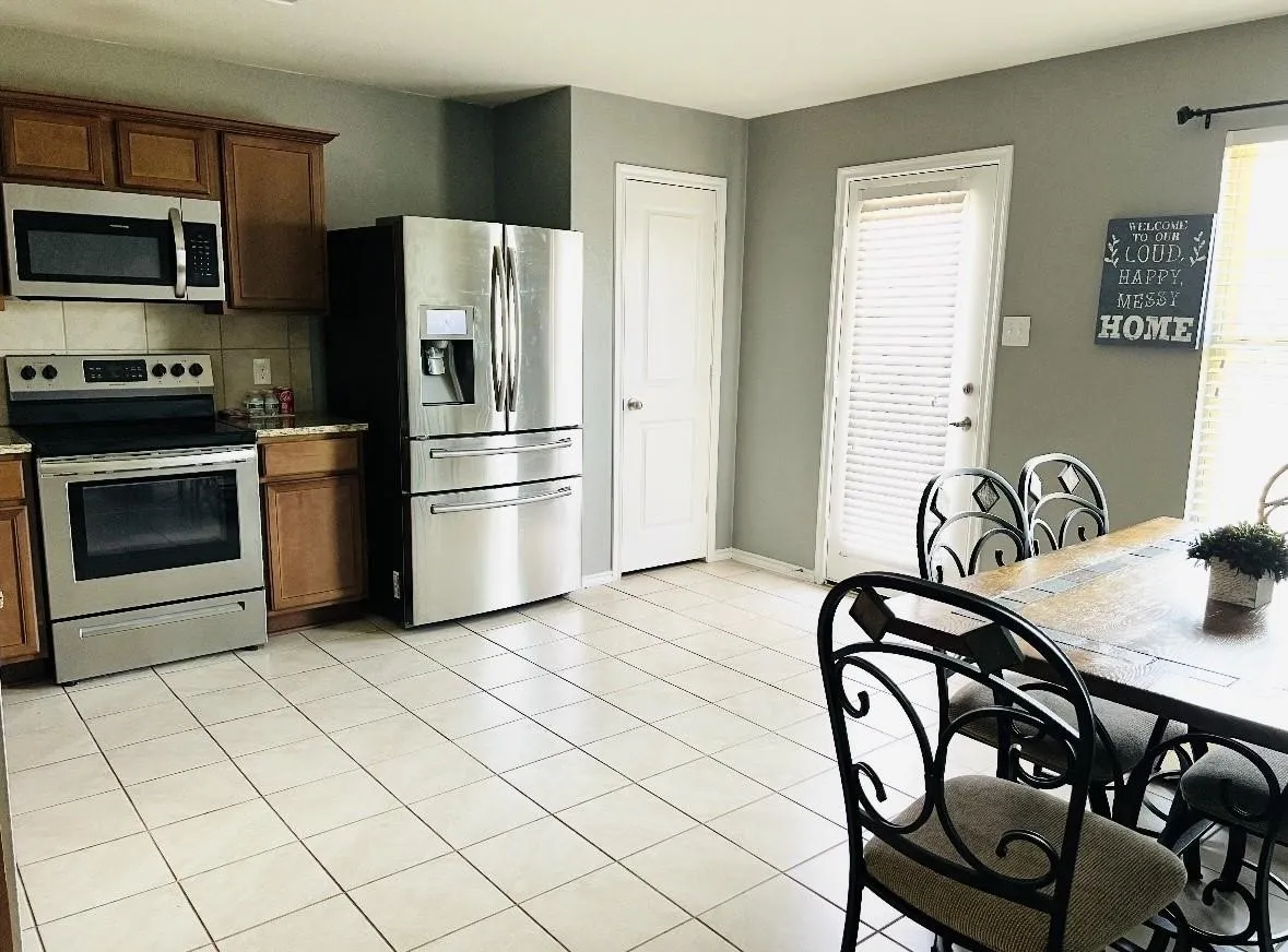 Kitchen featuring stainless steel appliances, wood cabinetry, granite-finish countertops, and tile flooring