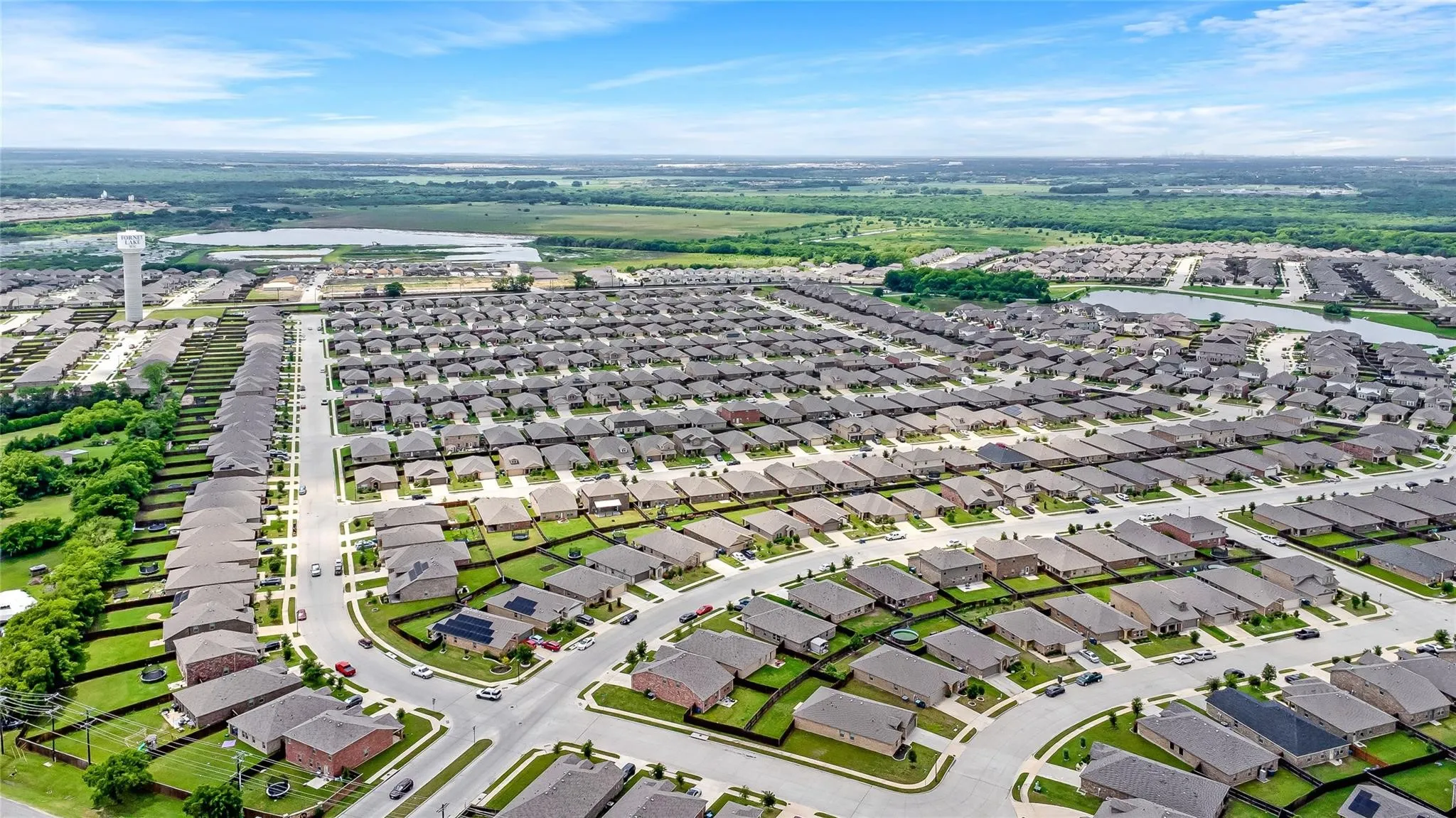 Aerial perspective of a large residential development featuring numerous single-story homes with dark roofs and light-colored exteriors