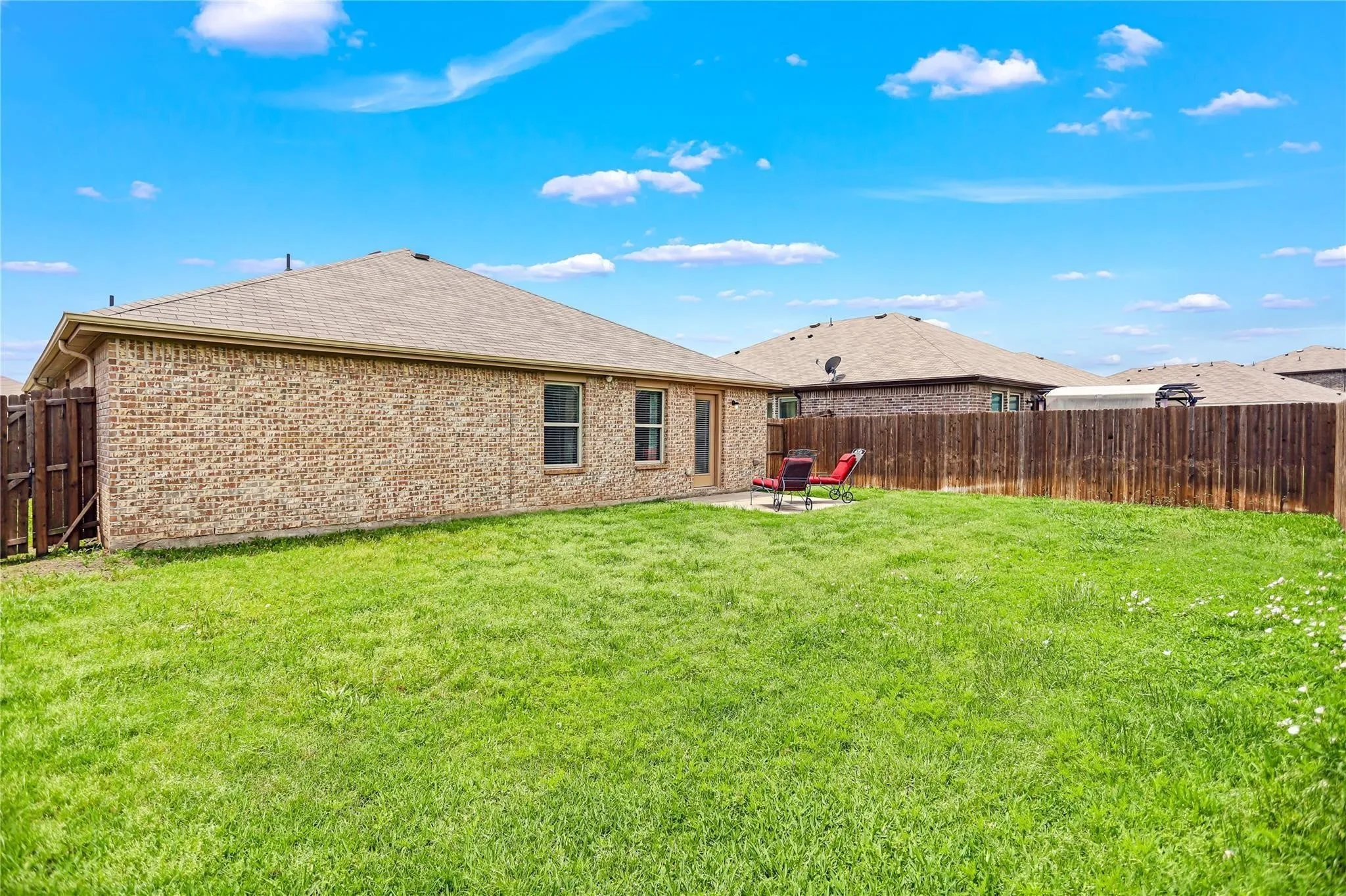 Expansive backyard featuring a manicured lawn, full privacy fencing, and a concrete patio
