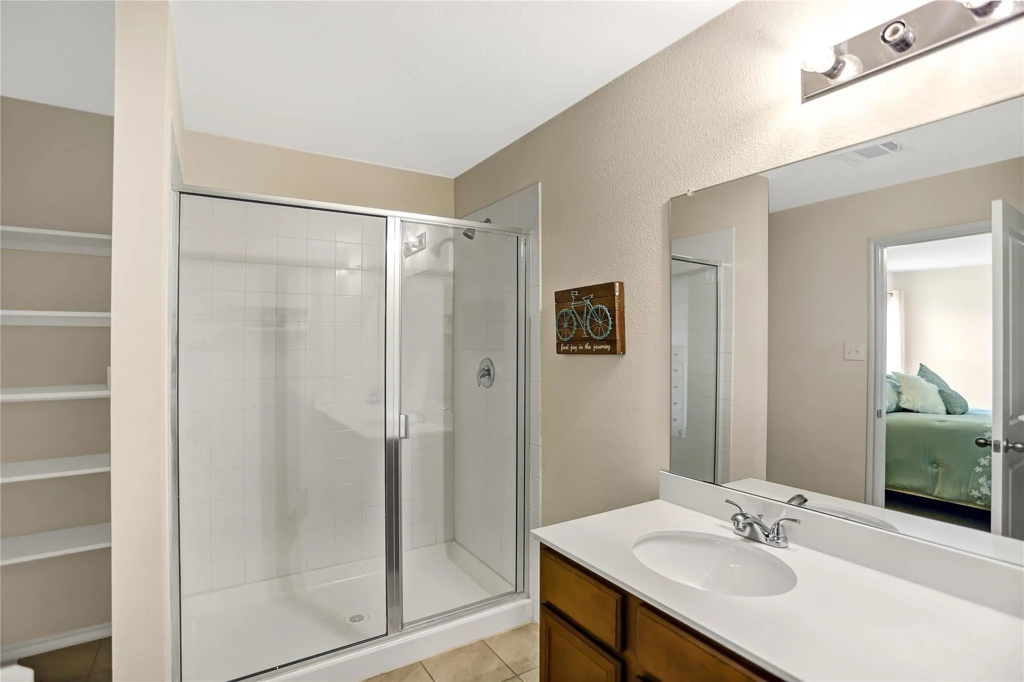 Bathroom featuring a glass-enclosed shower with subway tile, a single vanity with an integrated sink, a large wall-mounted mirror, and built-in shelving