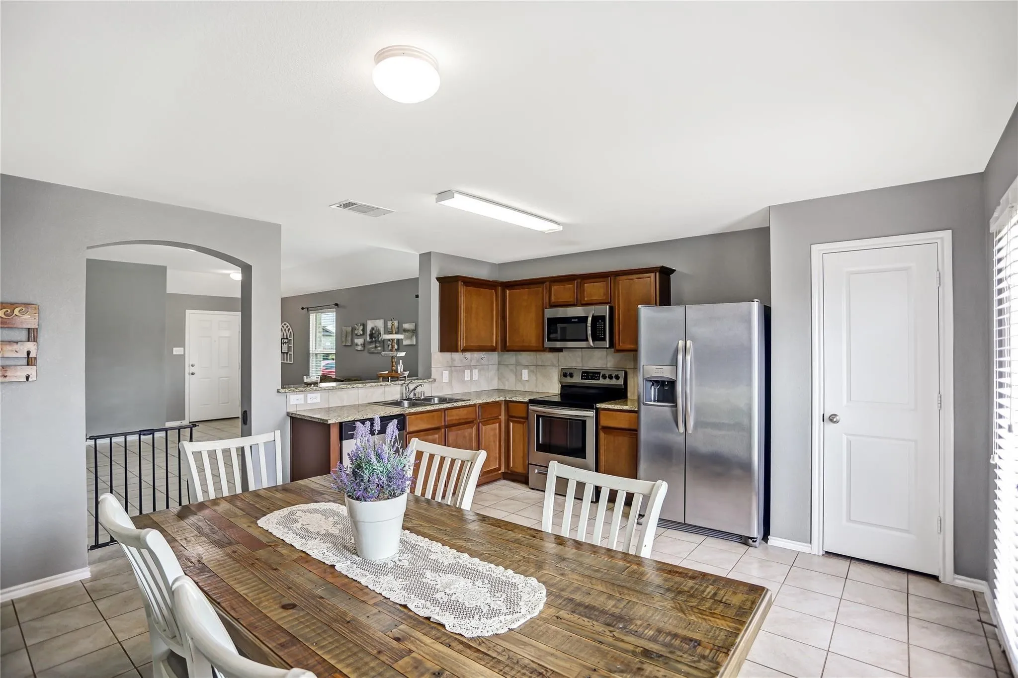 Spacious kitchen and dining area featuring stainless steel appliances, wood cabinetry, light countertops, and tile flooring