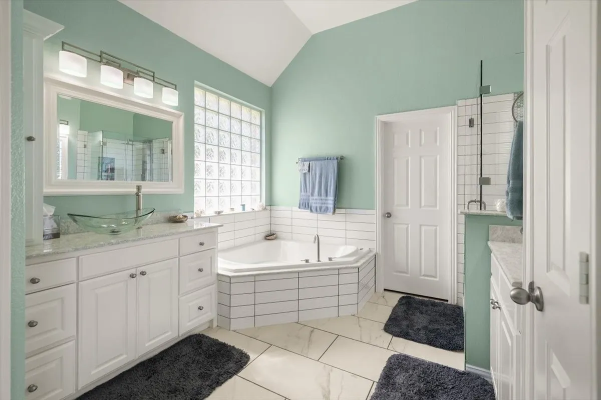 Bathroom featuring a corner soaking tub, glass block window, and dual vanities