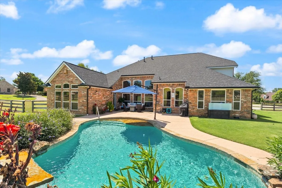 Rear exterior featuring a brick facade, shingled roof, and an in-ground swimming pool