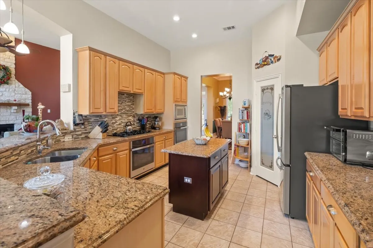 Kitchen featuring light wood cabinetry, granite countertops, a built-in oven, gas cooktop, and a matching granite-topped island