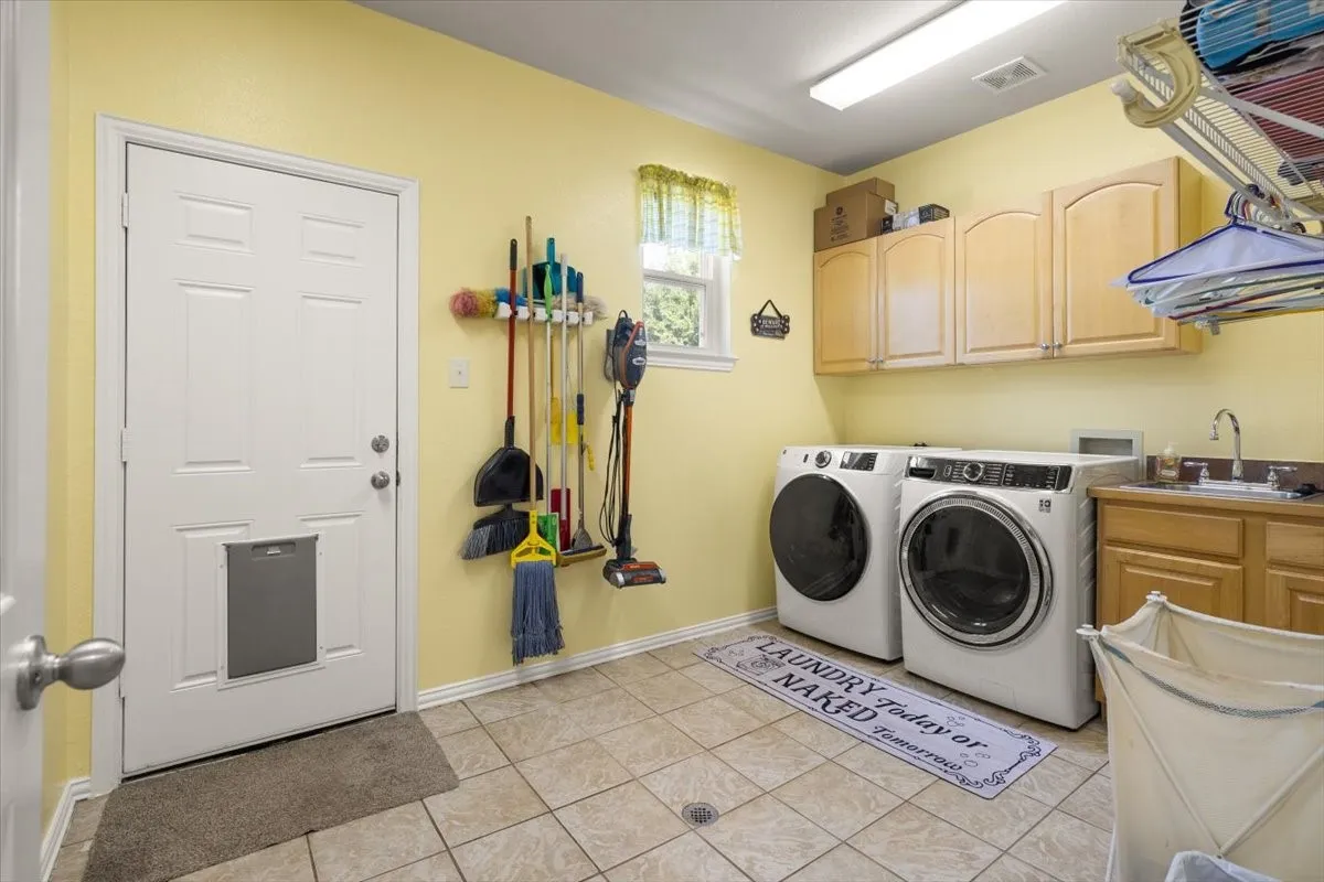 Dedicated laundry room featuring light-toned cabinetry, a utility sink, and tile flooring