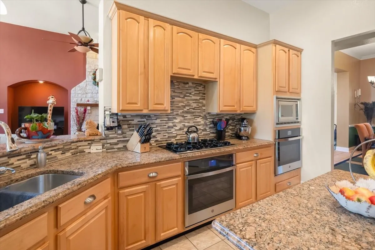 Kitchen featuring light wood cabinetry with brushed nickel hardware, granite countertops, stainless steel appliances, and a mosaic tile backsplash