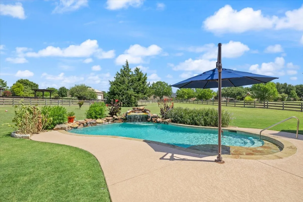 Backyard swimming pool with rock waterfall feature, integrated spa, and expansive concrete decking