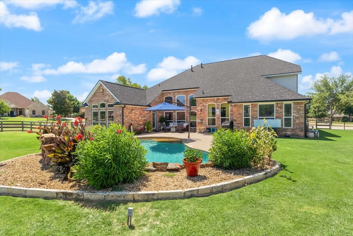 Rear exterior featuring a brick facade, shingled roof, and an in-ground swimming pool