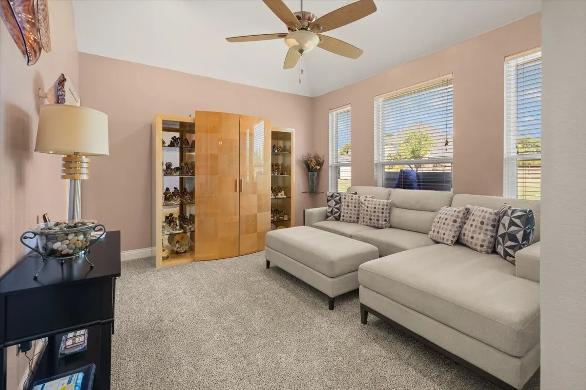 Carpeted living space with a vaulted ceiling, ceiling fan, and multiple windows with blinds