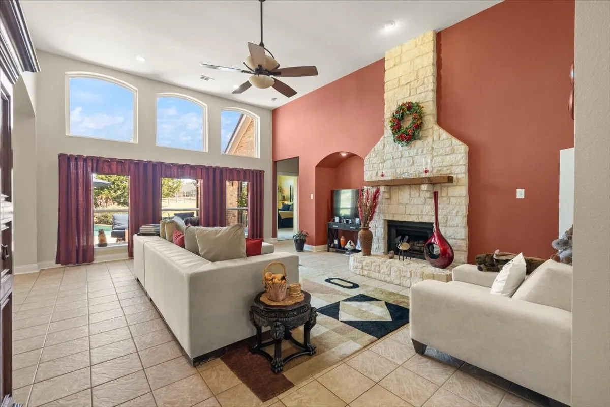 Great room featuring a floor-to-ceiling stone fireplace with a wood mantle, high ceilings, arched windows, and tiled flooring