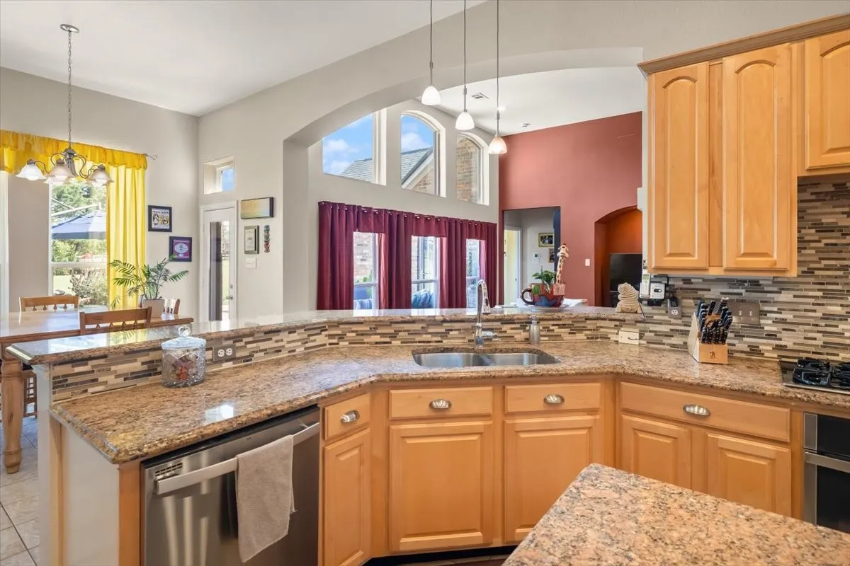 Kitchen featuring a double basin sink, light wood cabinetry, stone-finish countertops, and a mosaic tile backsplash
