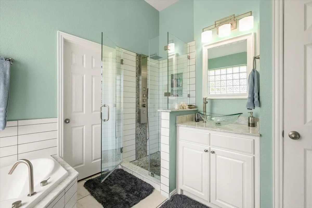 Bathroom featuring a glass-enclosed shower, corner soaking tub, and a vanity with a vessel sink
