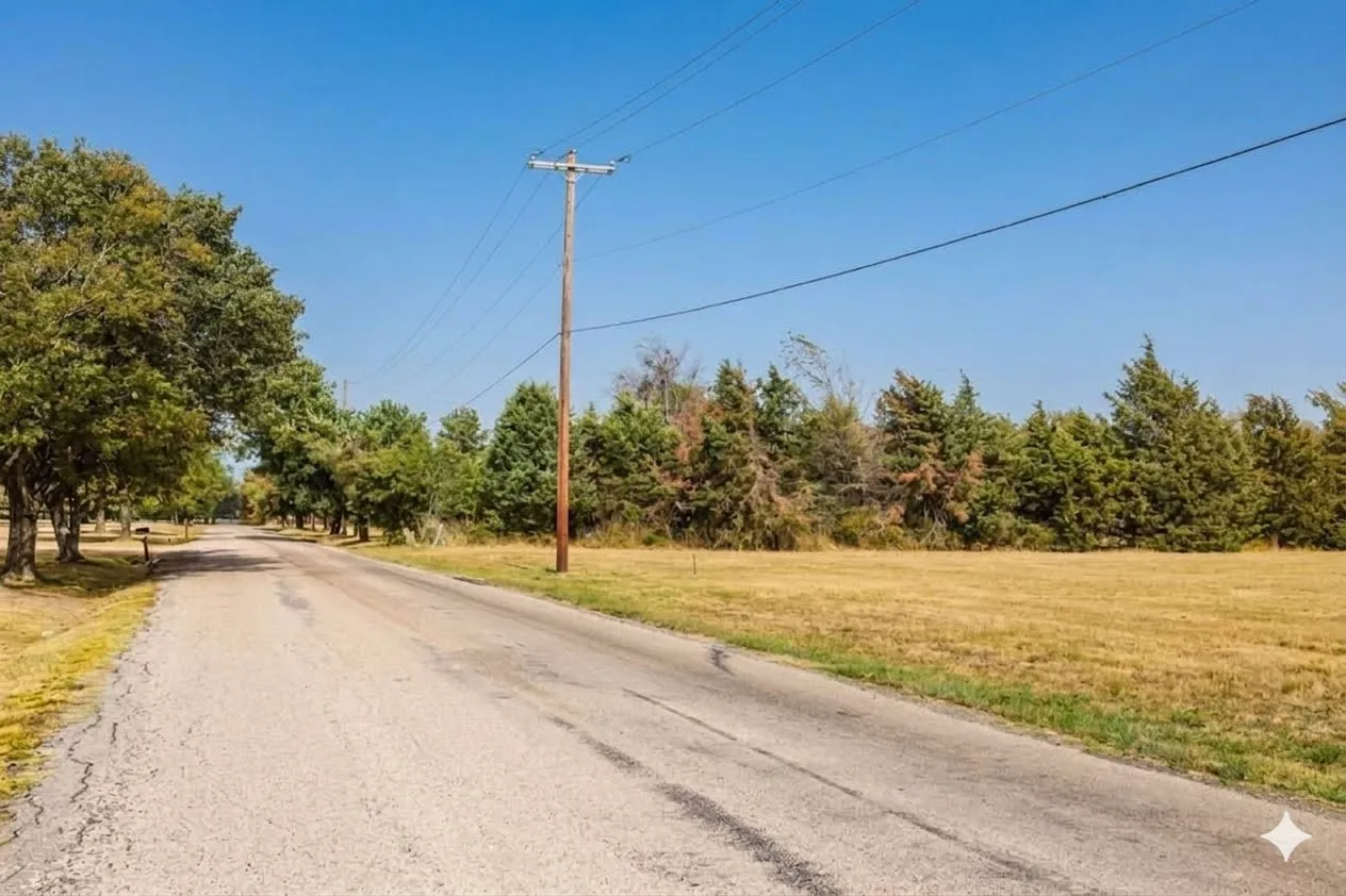 Paved road entrance bordered by mature trees and a substantial grassy expanse