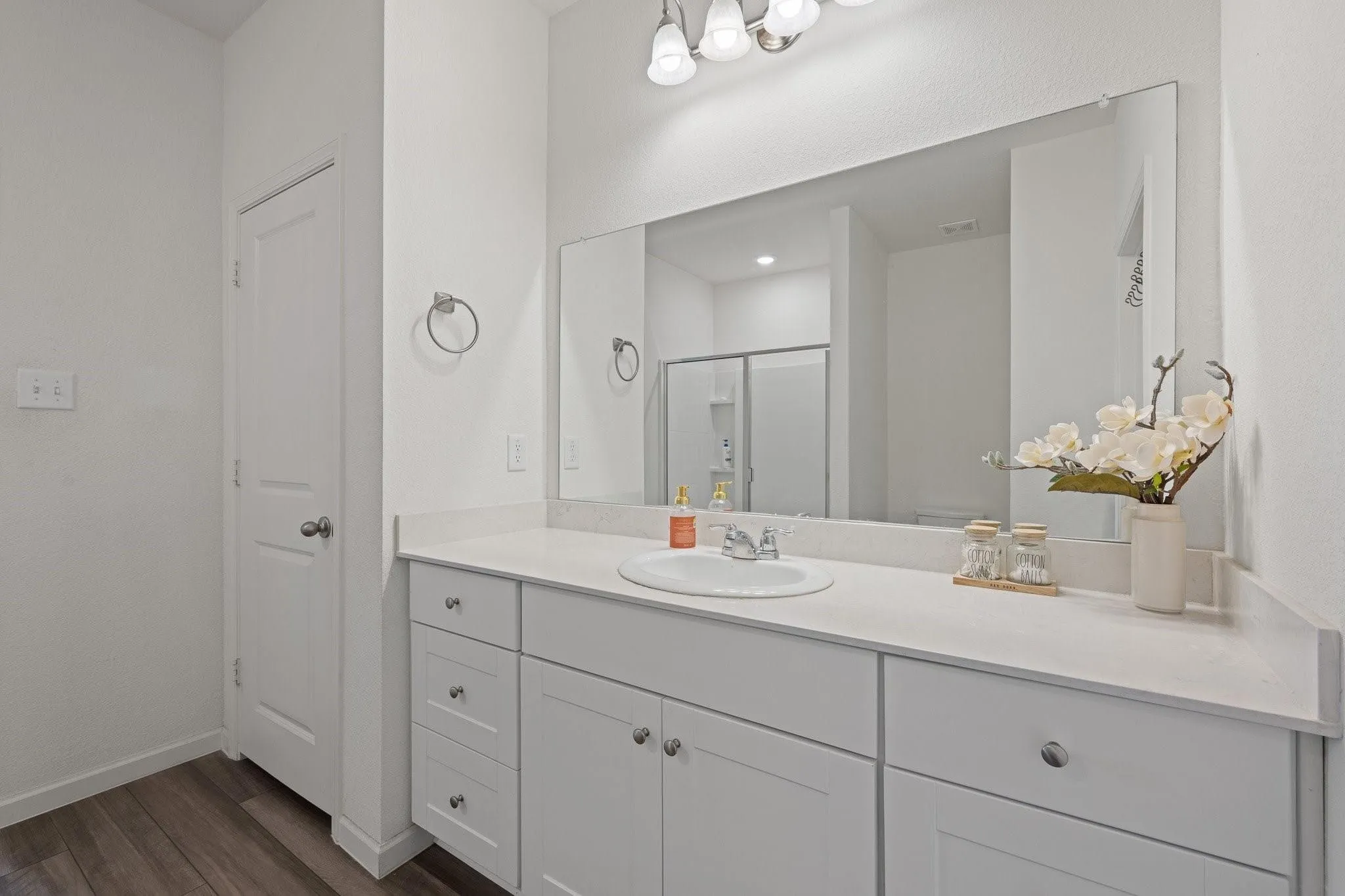Full bathroom view with dual-sink vanity, gray cabinetry, a large mirror, and clean white finishes throughout.
