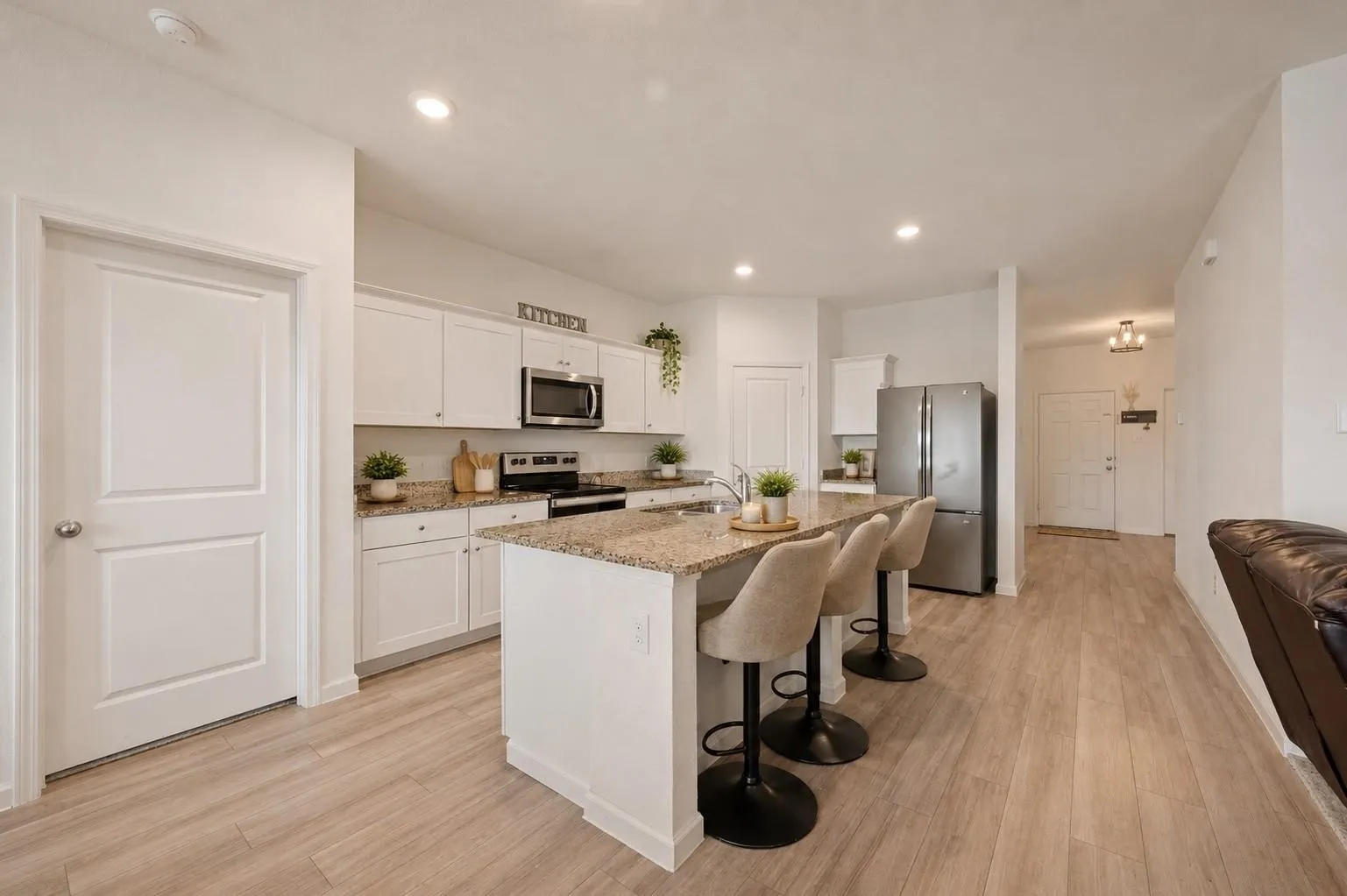 Second kitchen view highlighting the open layout, white cabinetry, and seamless flow into the main living areas. Decor is Virtually Staged
