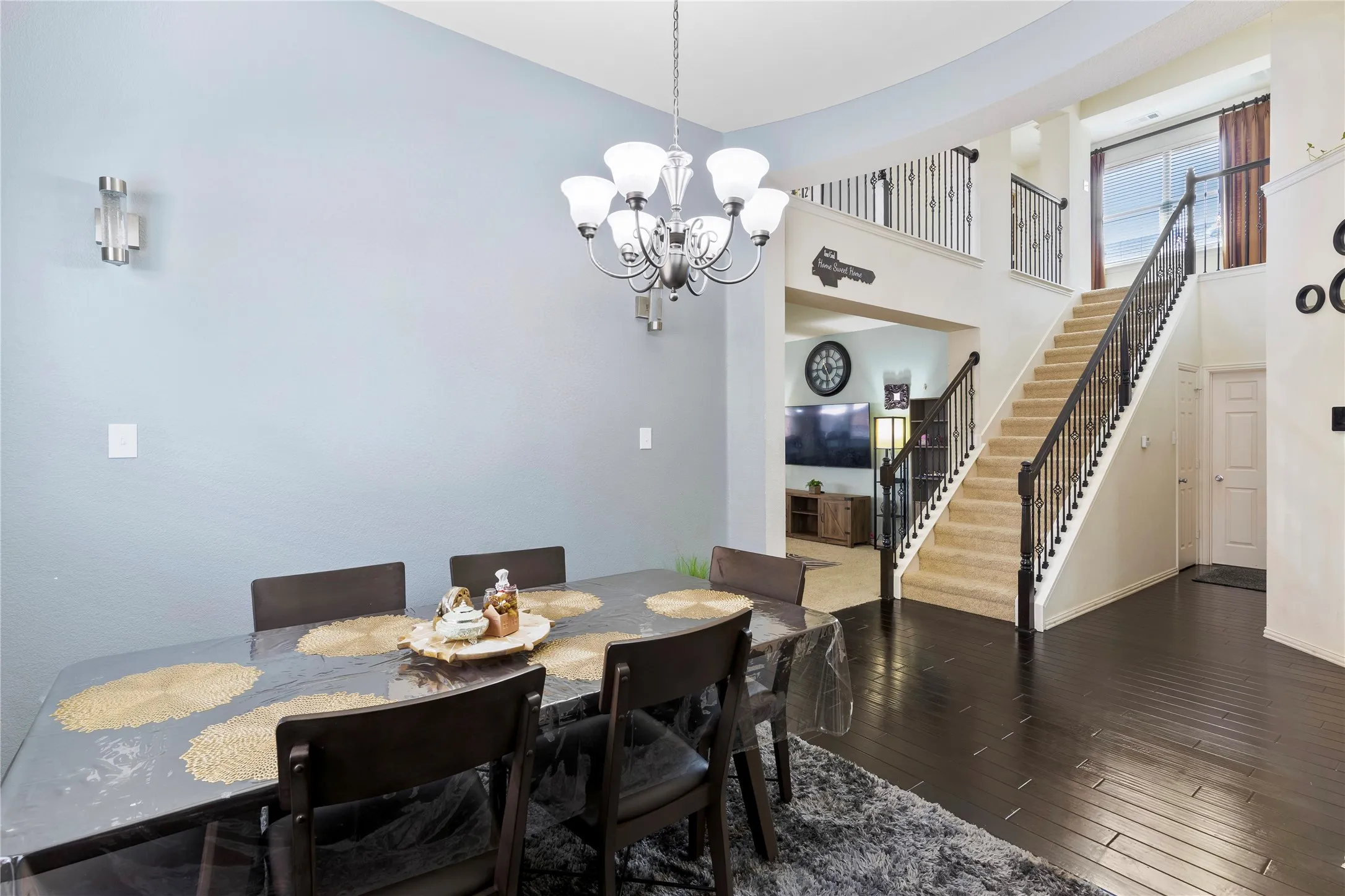 Open-concept interior featuring dark wood-finish flooring, a grand staircase with wrought iron balusters, a second-story landing with matching balusters, a multi-light chandelier, and recessed lighting