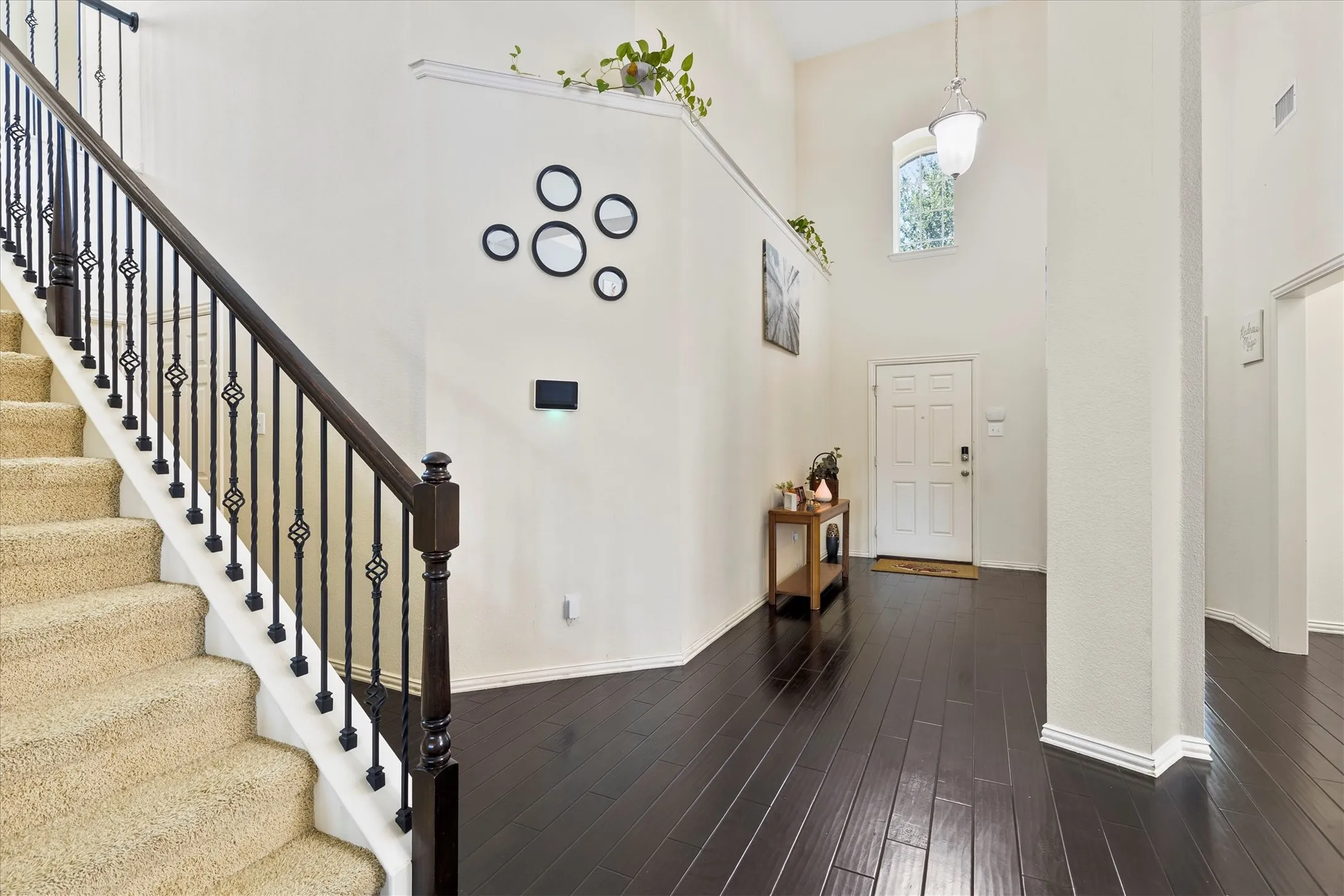 Foyer featuring dark wood-finish flooring, a carpeted staircase with wrought iron balusters, a vaulted ceiling, and an arched transom window above the entry door