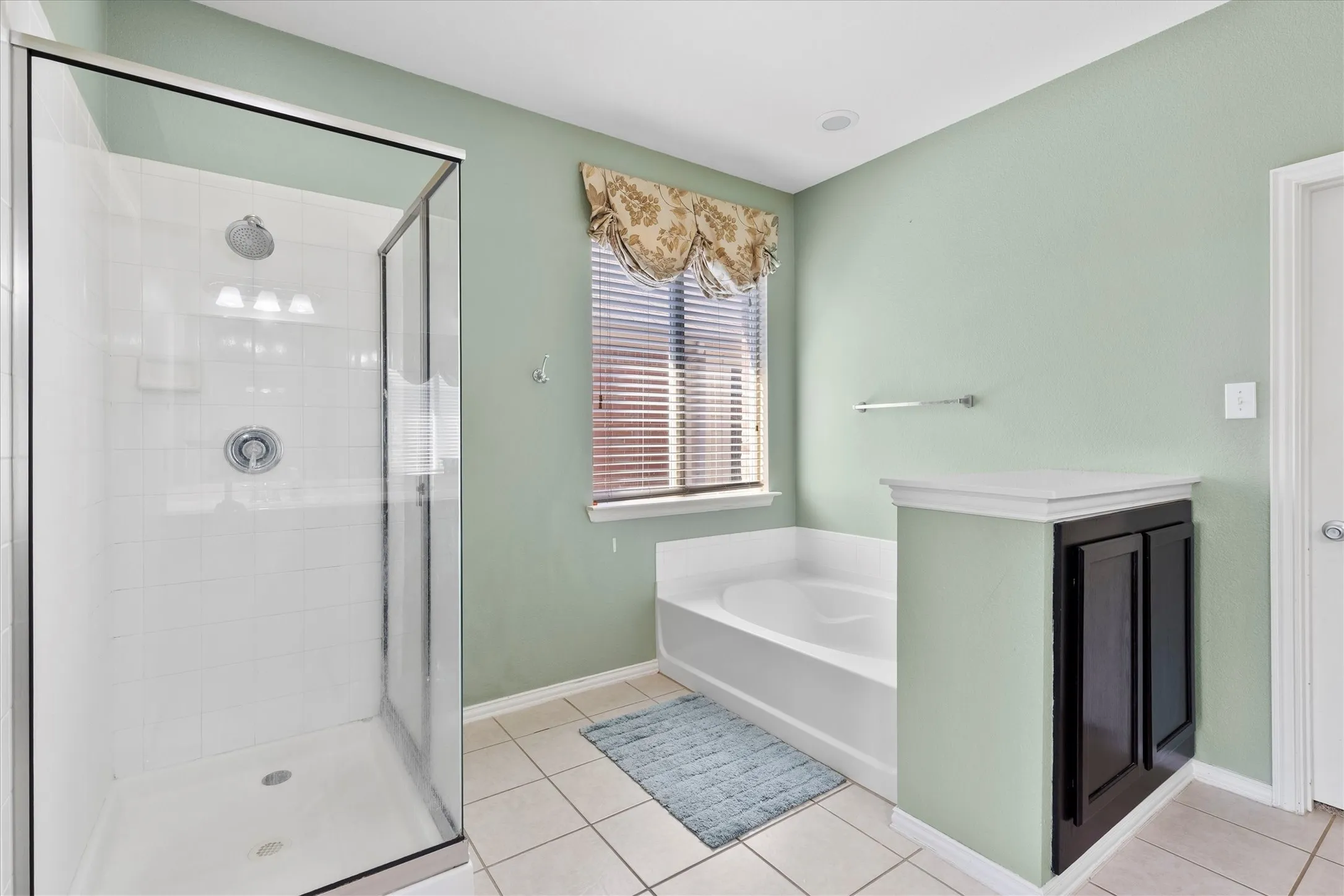 Bathroom featuring a glass-enclosed shower with white tiled walls, a built-in soaking tub, a window with blinds, and a built-in storage cabinet with a white countertop