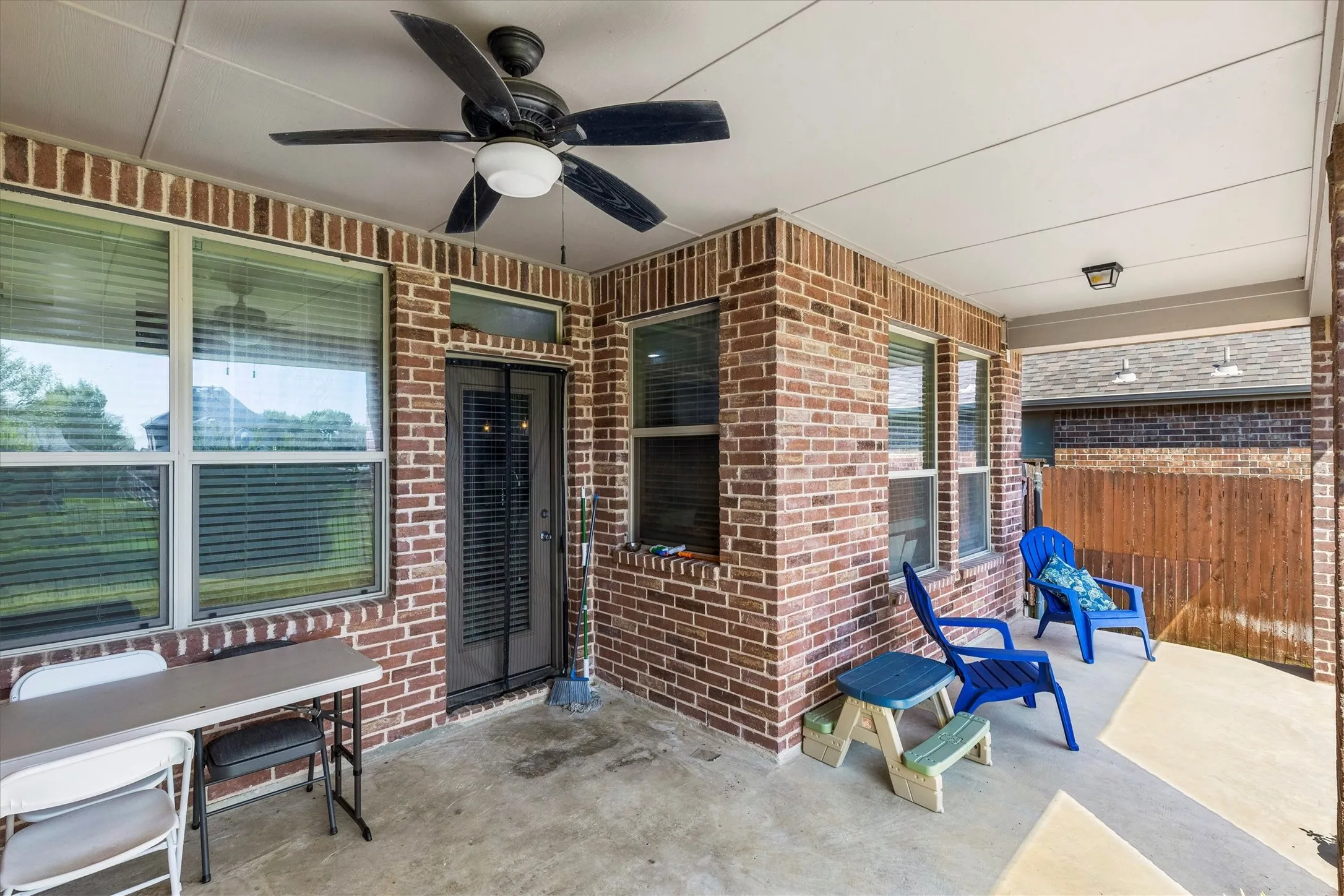 Covered patio featuring a ceiling fan, concrete flooring, and brick exterior walls