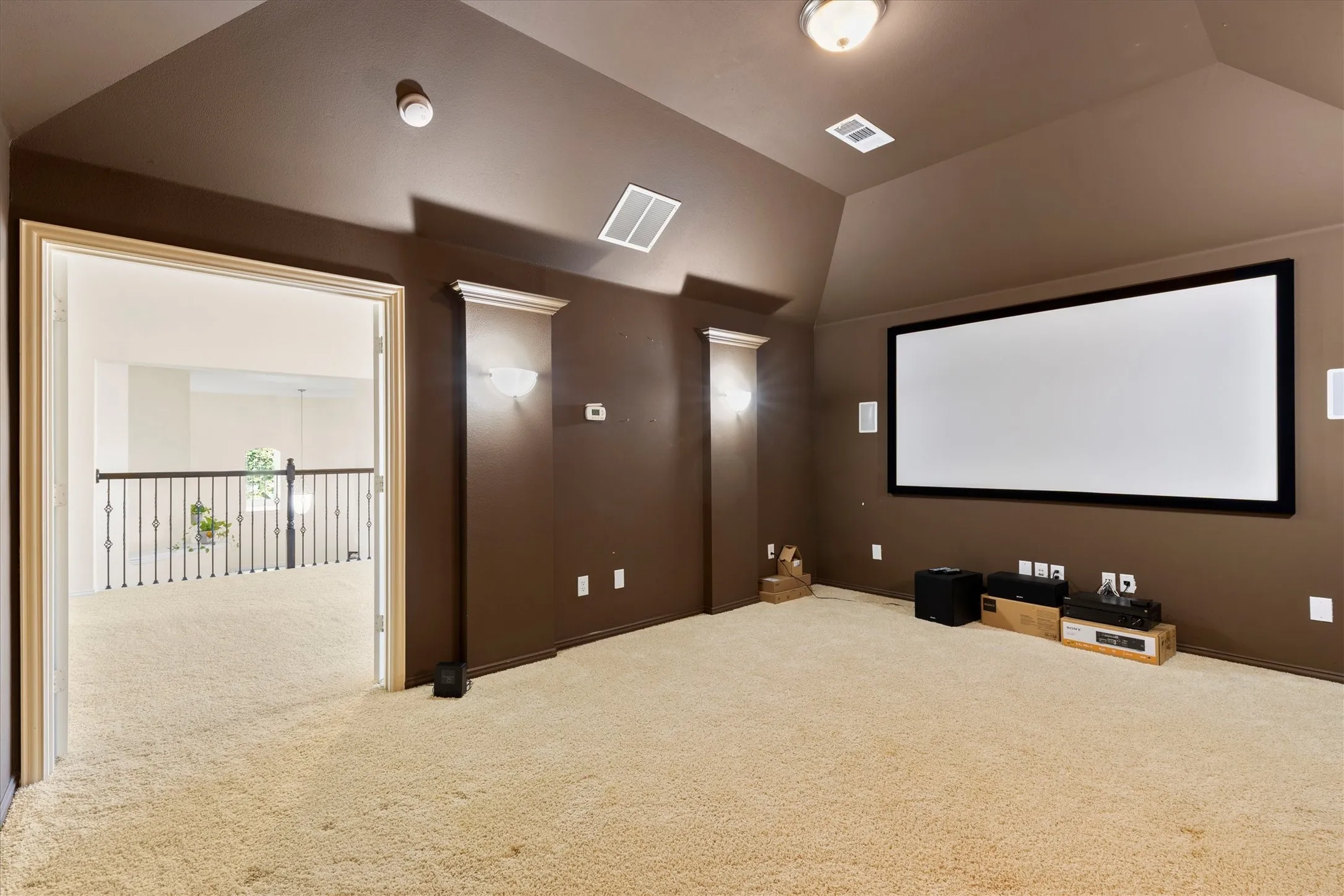 Dedicated media room featuring a large projection screen, recessed ceiling lighting, and wall-mounted sconces