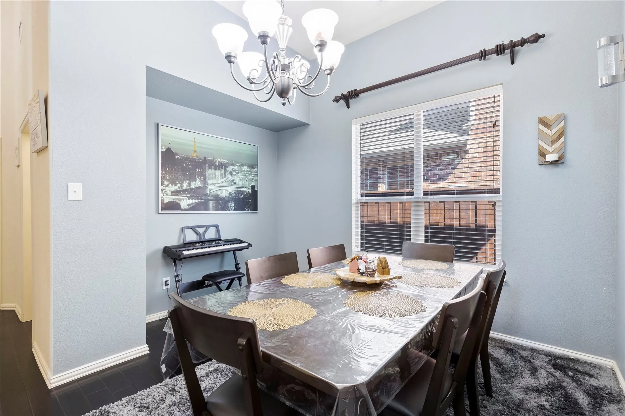 Dining area featuring dark wood-finish flooring, a contemporary chandelier, recessed wall niche, and a window with blinds