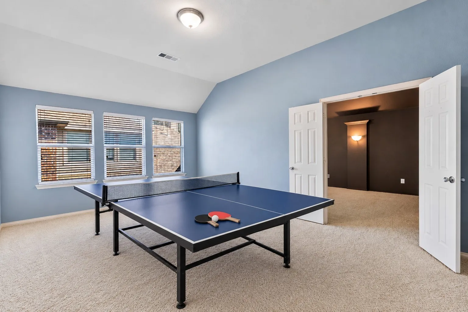 Carpeted room with three windows featuring blinds, a vaulted ceiling, and an open doorway to an additional carpeted space