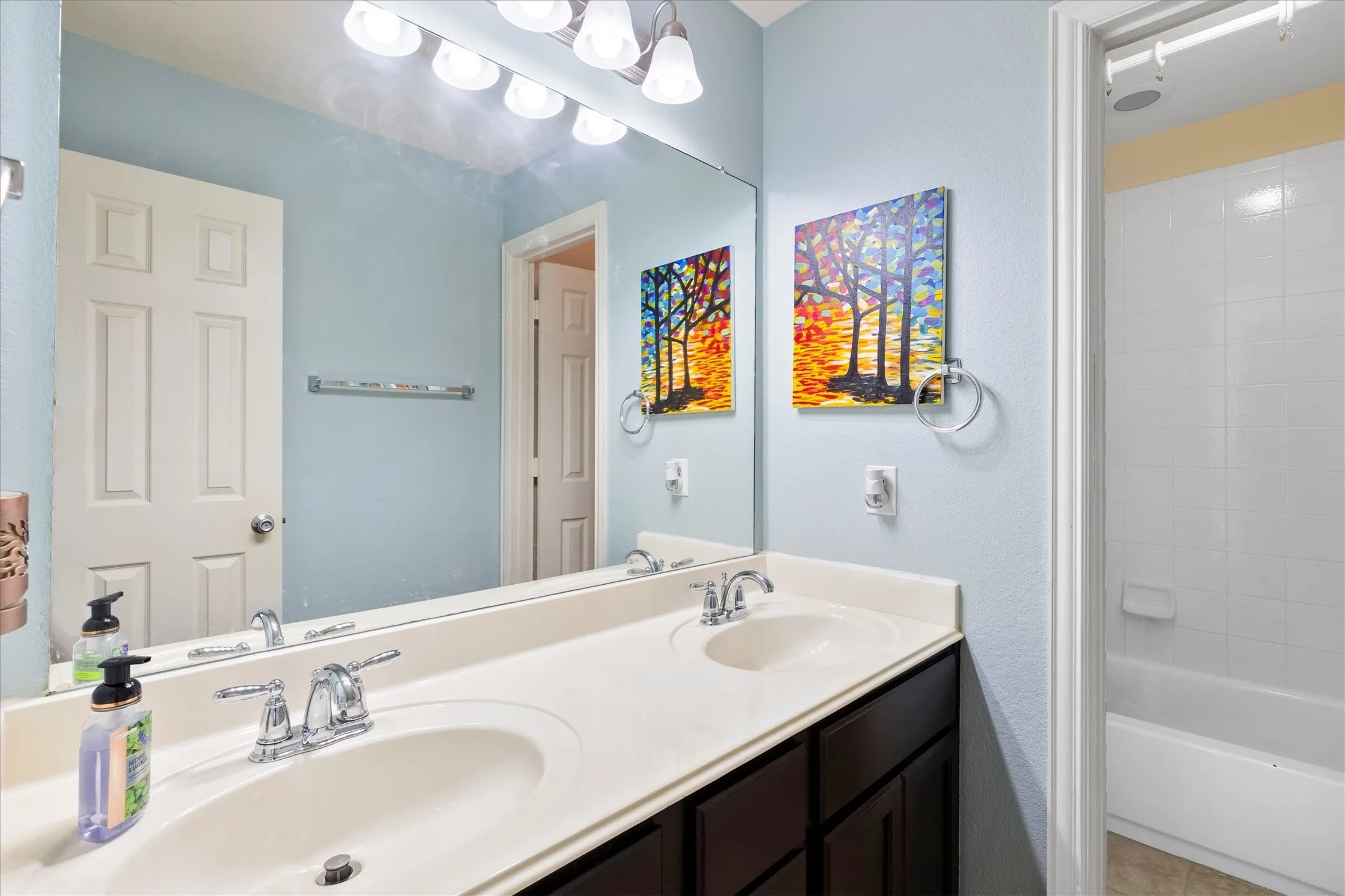 Vanity with dual integrated sinks and chrome faucets, complemented by an expansive wall-mounted mirror