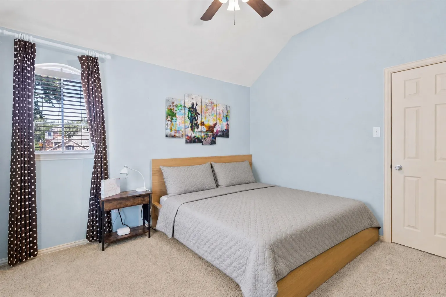 Arched window with blinds, vaulted ceiling, neutral carpet, and ceiling fan