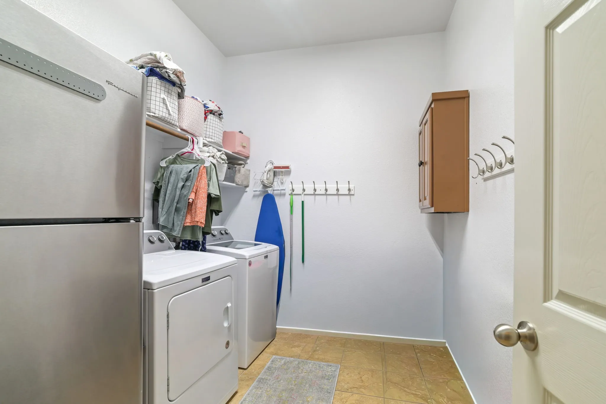 Laundry area featuring tile flooring, white walls, built-in shelving, and a wall-mounted cabinet