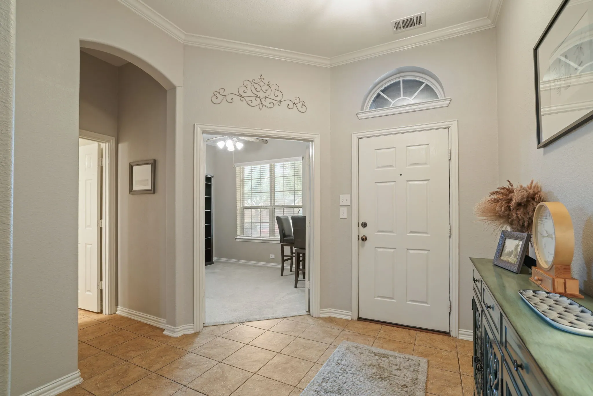 Entryway featuring a paneled door with an arched transom window, ceramic tile flooring, and a cased opening leading to a carpeted room with multiple windows